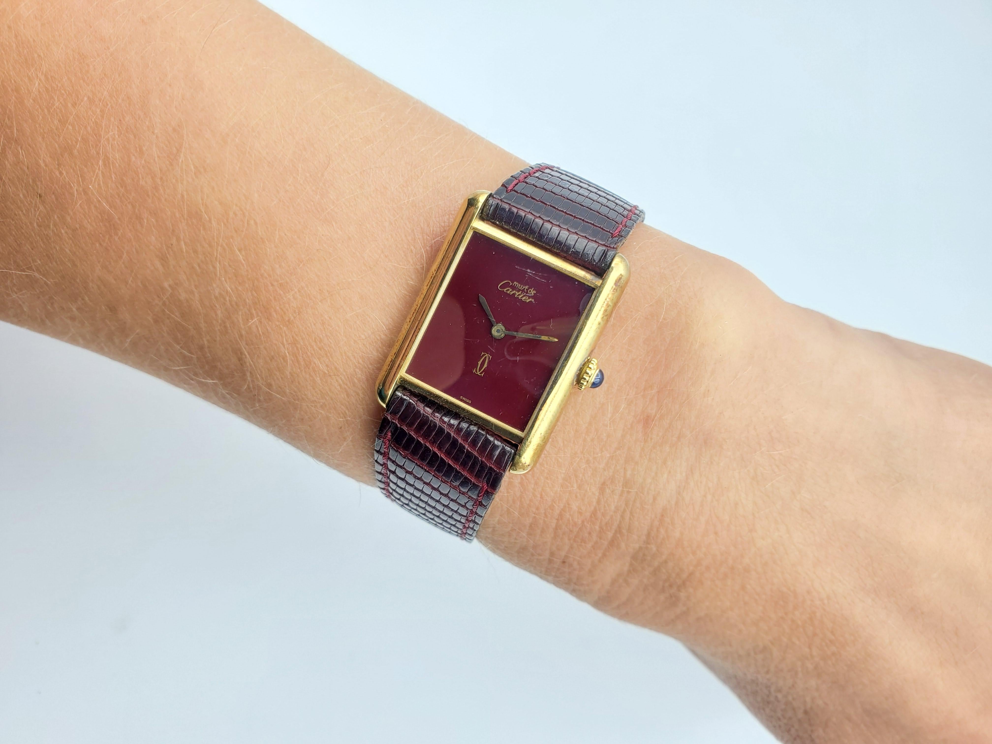 Cartier Must De Watch, Tank Vermeil. The watch has a burgundy/brown color. Estimated in the 1970s. The length is 8.5 inches total. Very minor scratch on crystal. The strap is aftermarket. The case is 23 x 23 mm and 6.4mm thick. Cabochon sapphire