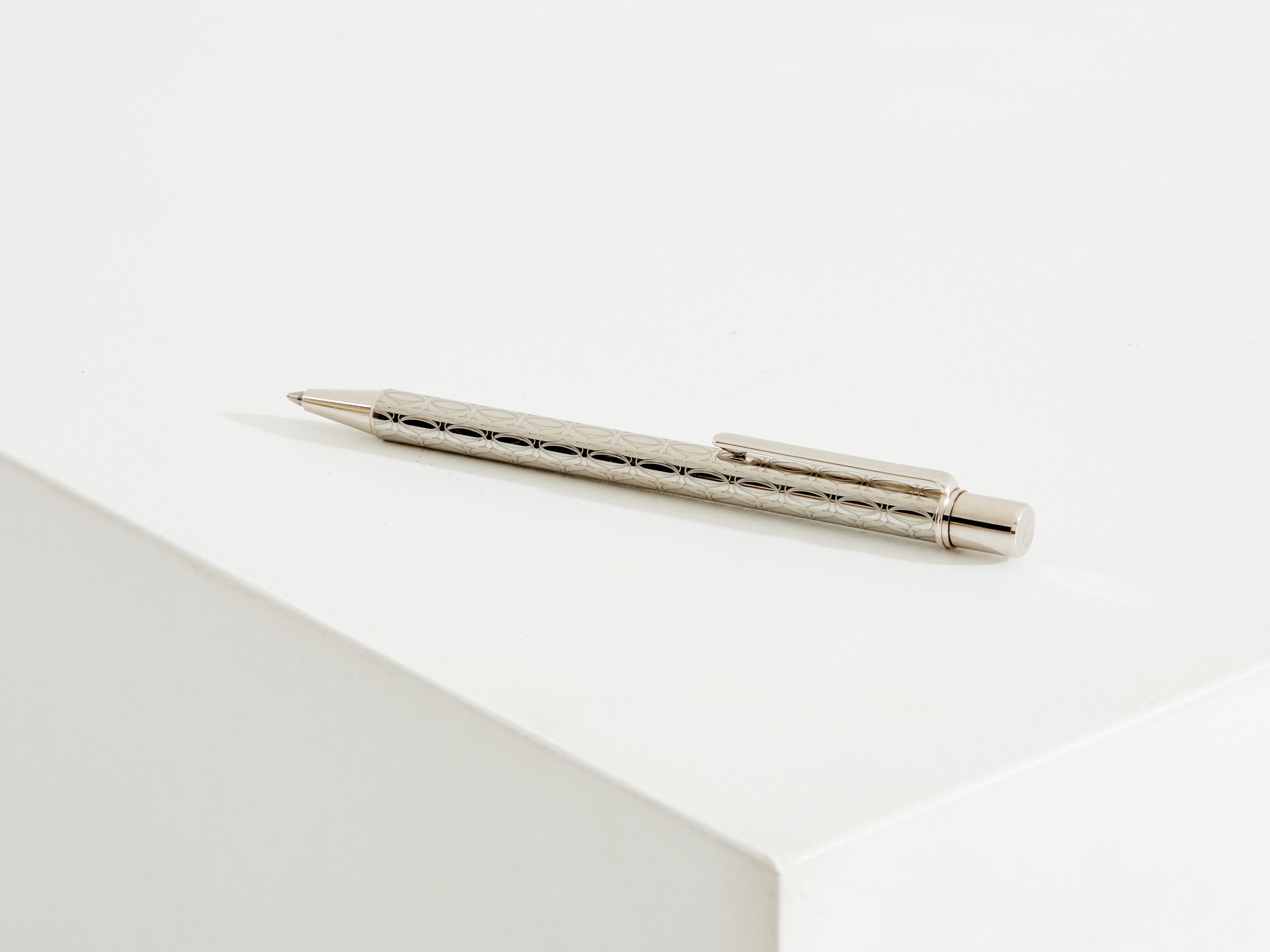 This Cartier Must II ballpoint pen from the 1980s is a rare piece made of silver plating and palladium, adorned with a distinctive engraved motif featuring Cartier's iconic 