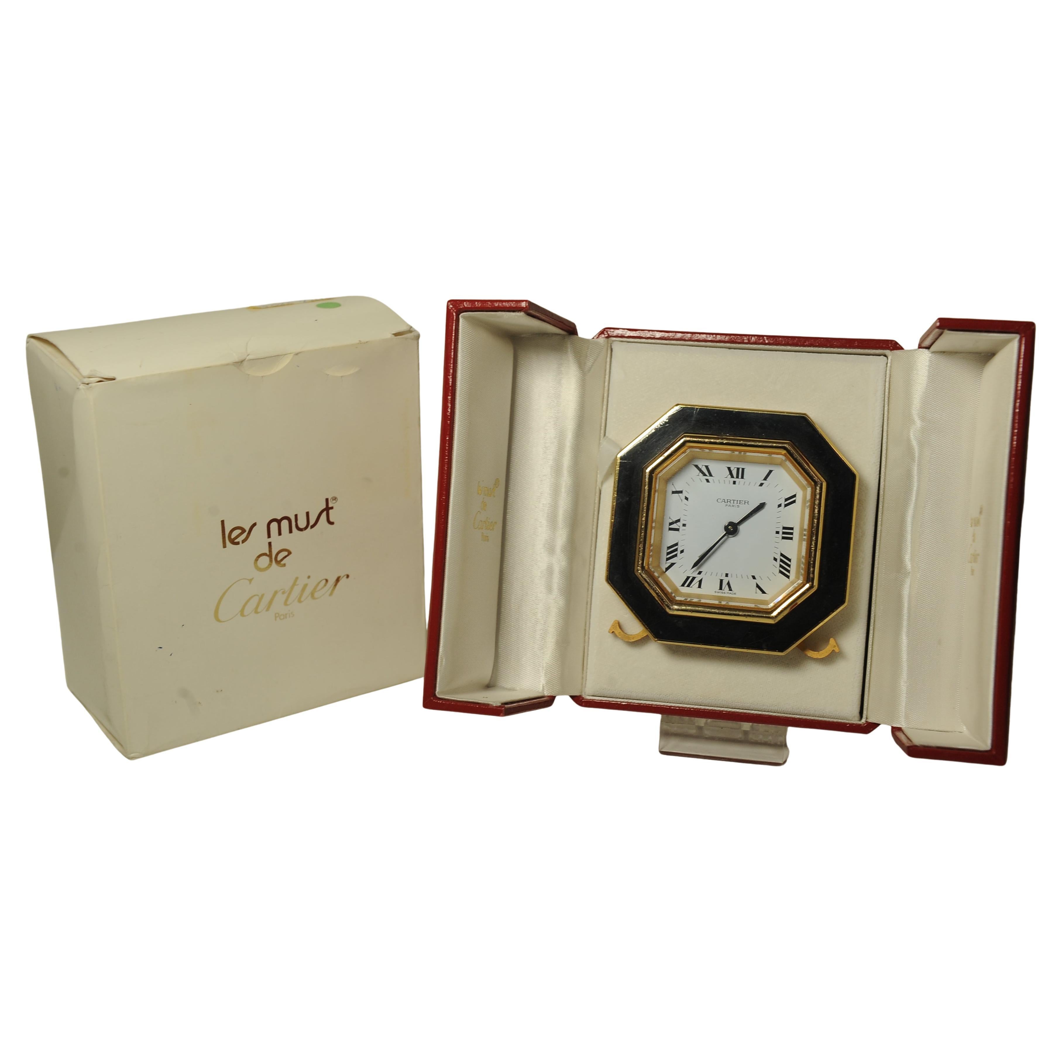 A Cartier Octagonal Mechanical 8-day Movement Desk Clock Gilt Metal and Black Enamel Table Alarm Clock With White Dial & Roman Numerals 

Made in Switzerland Number 7507 16915

Supplied With Red Cartier Two Door Red Leather Box 

- Cartier Alarm