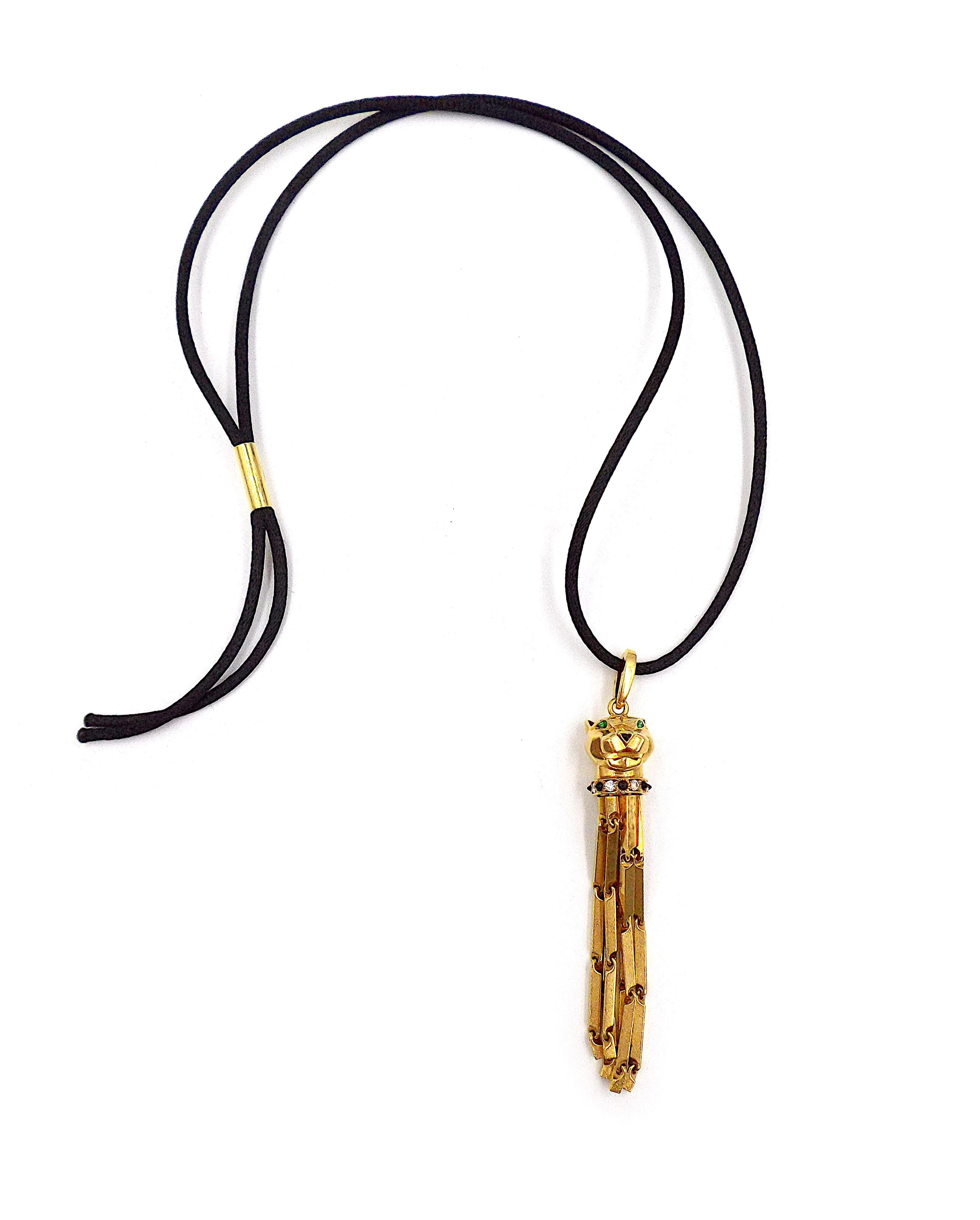 A modern Cartier necklace featuring a gold pendant shaped as a panther head with 6 long tassels on an original black cord with a gold sliding clasp. The pendant is decorated with onyx and diamonds, the panther head is set with tsavorite garnet