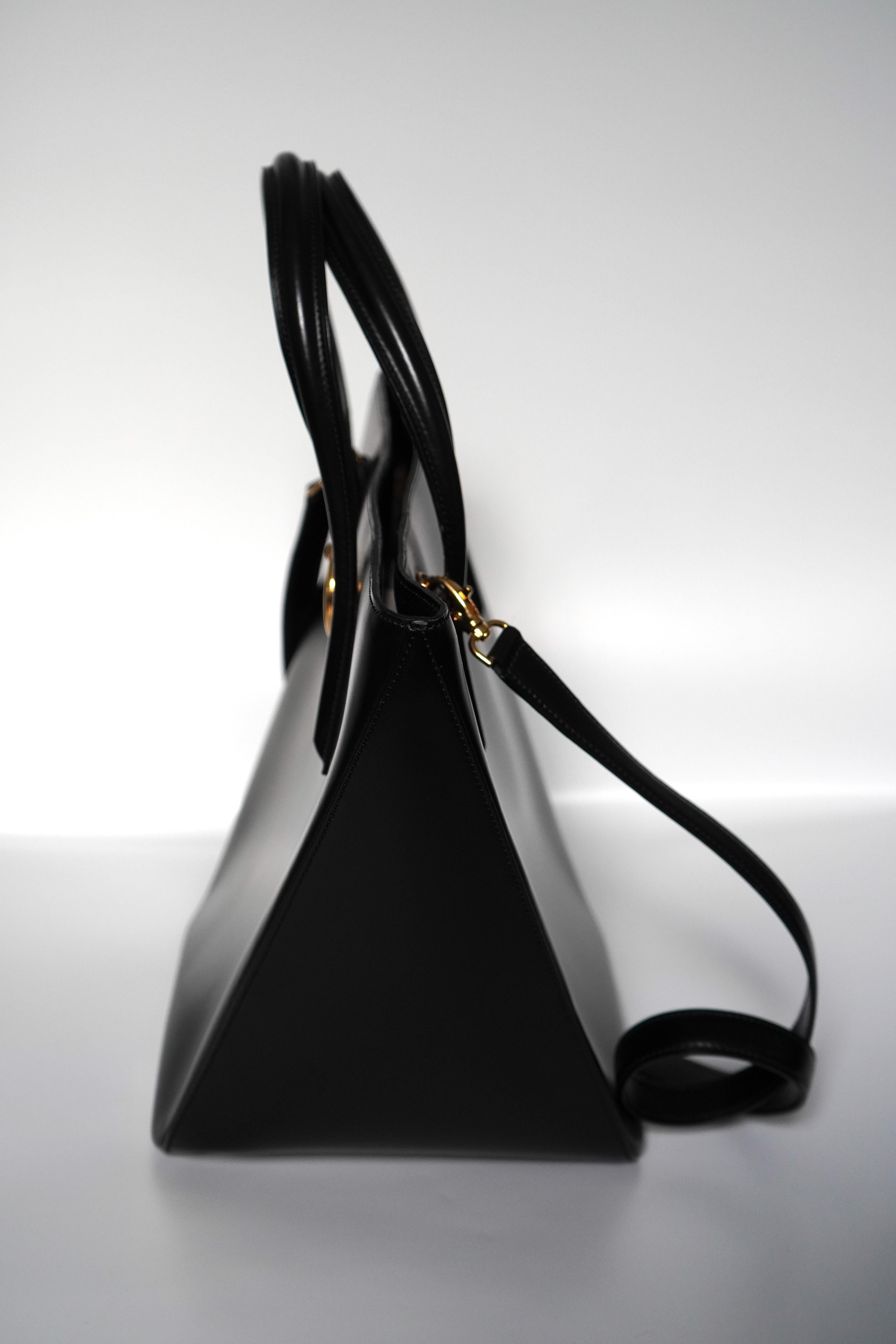 Black structured bag from Cartier with the
iconic Cartier panther ring detail. The inside of the bag features a dual zipper and open pocket, animal print lining, and a zip to close. The total height of the bag including the handles is 15 inches,