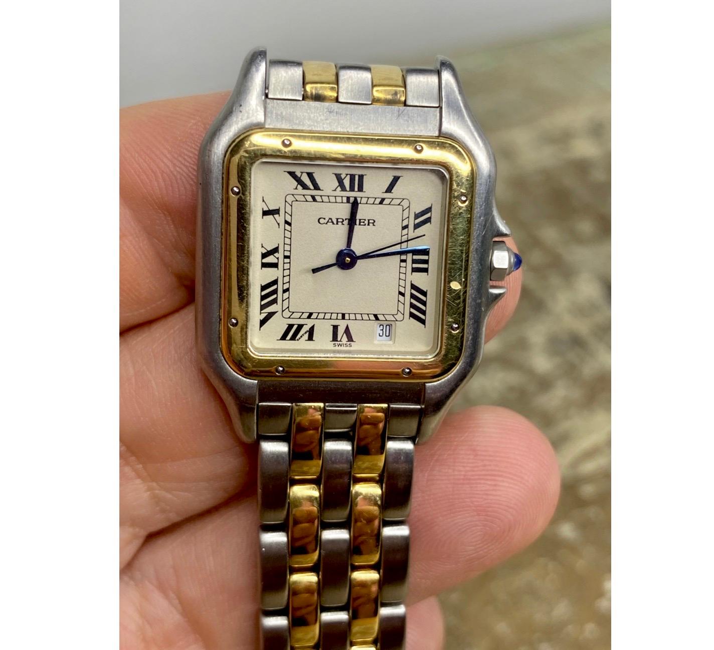 
Cartier Phantere
Midsize Ladies Watch. 
27mm stainless steel case with two-row 18K yellow gold bezel.
Off-White dial with blue steel hands and black Roman numerals hour markers. 
Date display at the 5 o'clock position. 
Two-tone stainless steel and