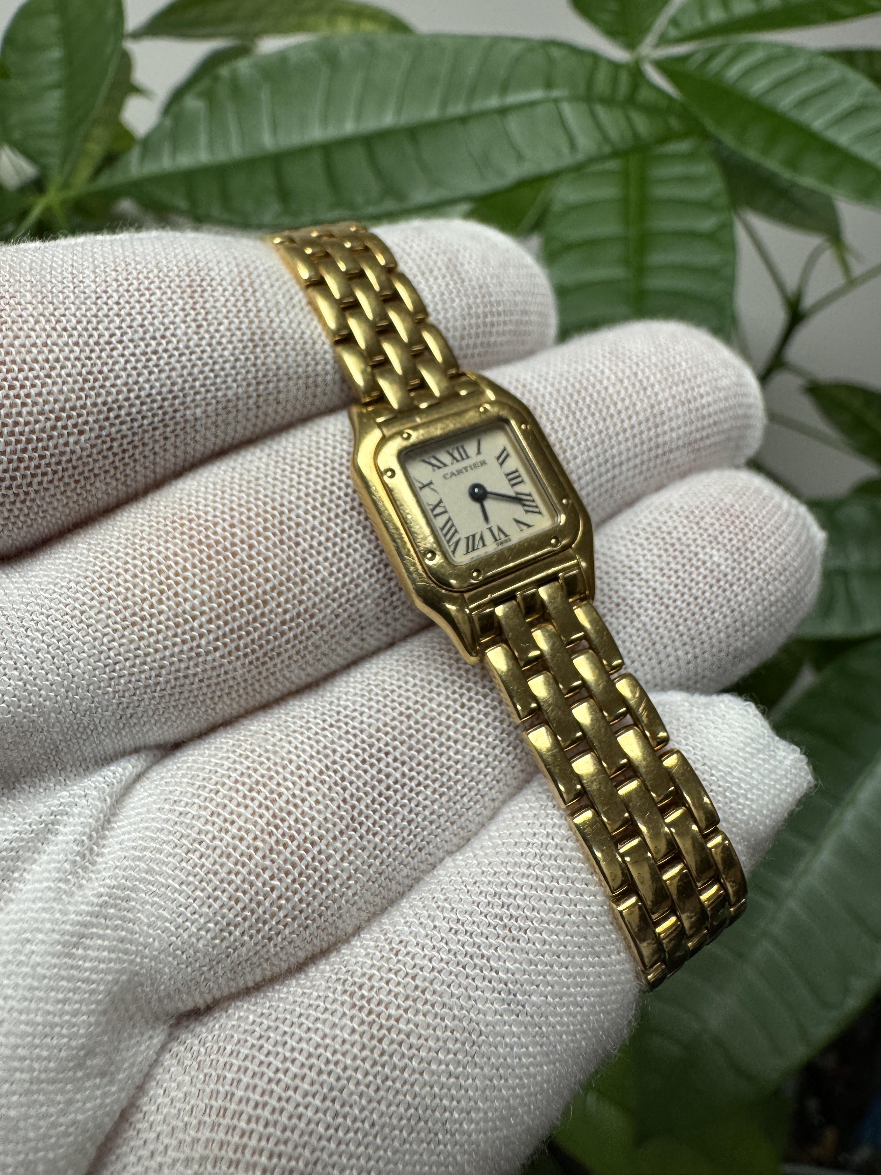 Montre Femme Cartier Panthère W25034B9 / 1130 Mini. Cette montre présente un boîtier de 17 mm en or jaune 18 carats et une lunette en or jaune 18 carats. Le cadran est ivoire avec des aiguilles bleues et des index en chiffres romains noirs. Il est