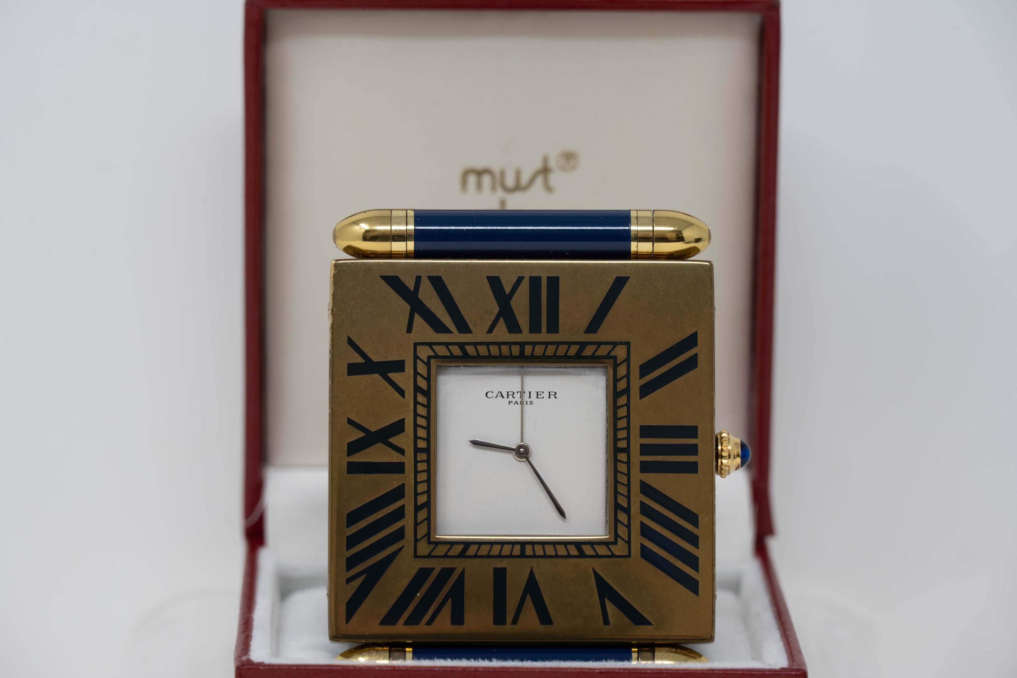 Cartier Paris alarm travel clock. Made in France, gold plated blue enamel outer bezel with box. Measures 2 5/8 inches x 2 inches, in good working order. Quartz movement, base #355109957. In good condition, tarnish base case.
