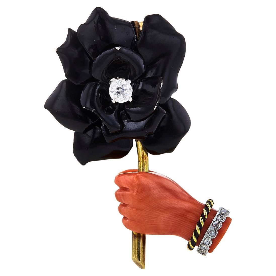 Authentic Cartier Paris clip-brooch crafted in 18 karat yellow gold, featuring a carved orangey red coral hand holding a black enamel flower centering an Old European Cut diamond weighing approximately .25 carats.  The coral hand is further enhanced