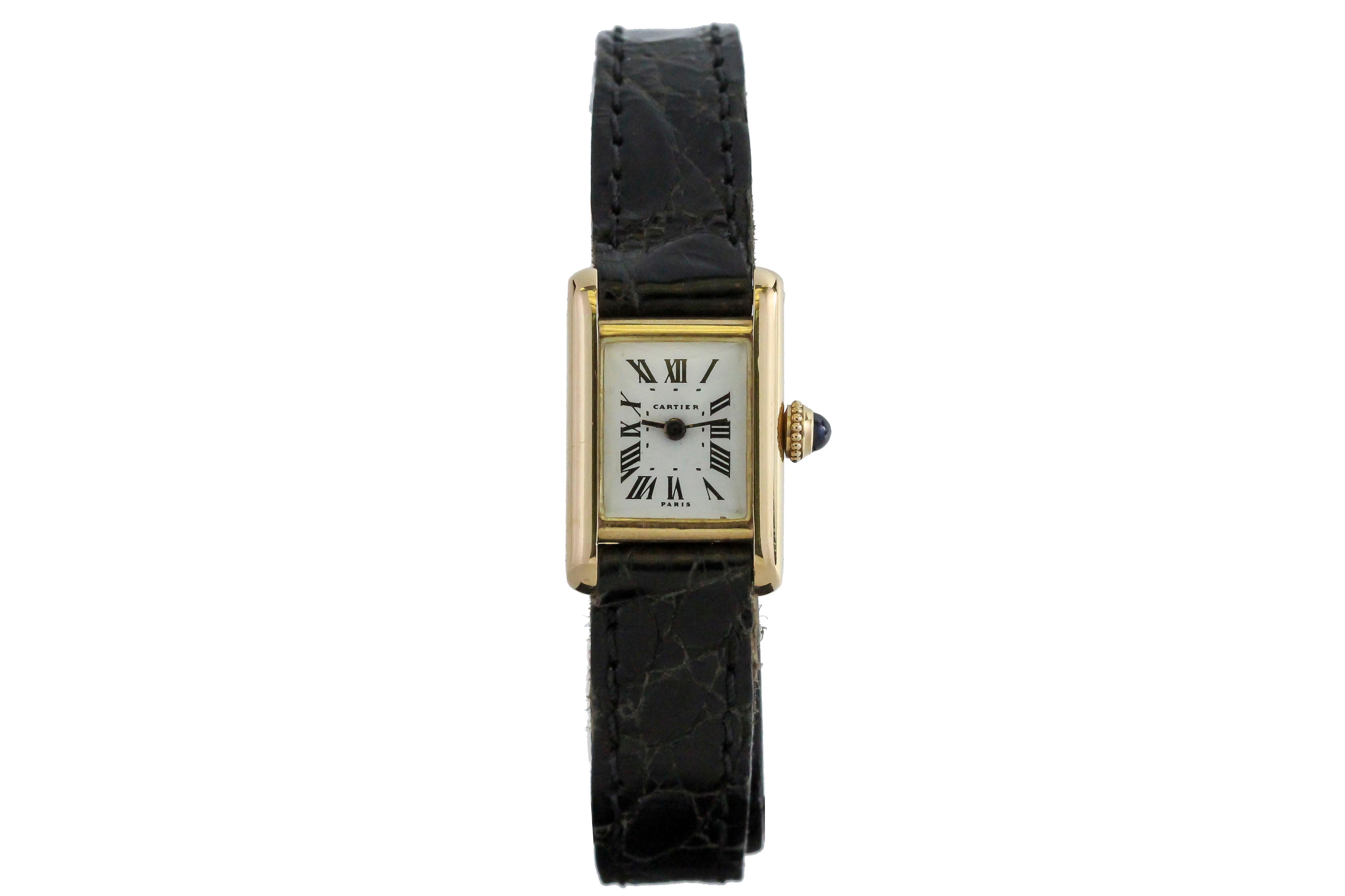 Cartier Paris Mini Tank in 18k yellow gold has a manual wind movement, cream dial with Roman numerals and is on a leather strap with a Cartier deployant clasp.