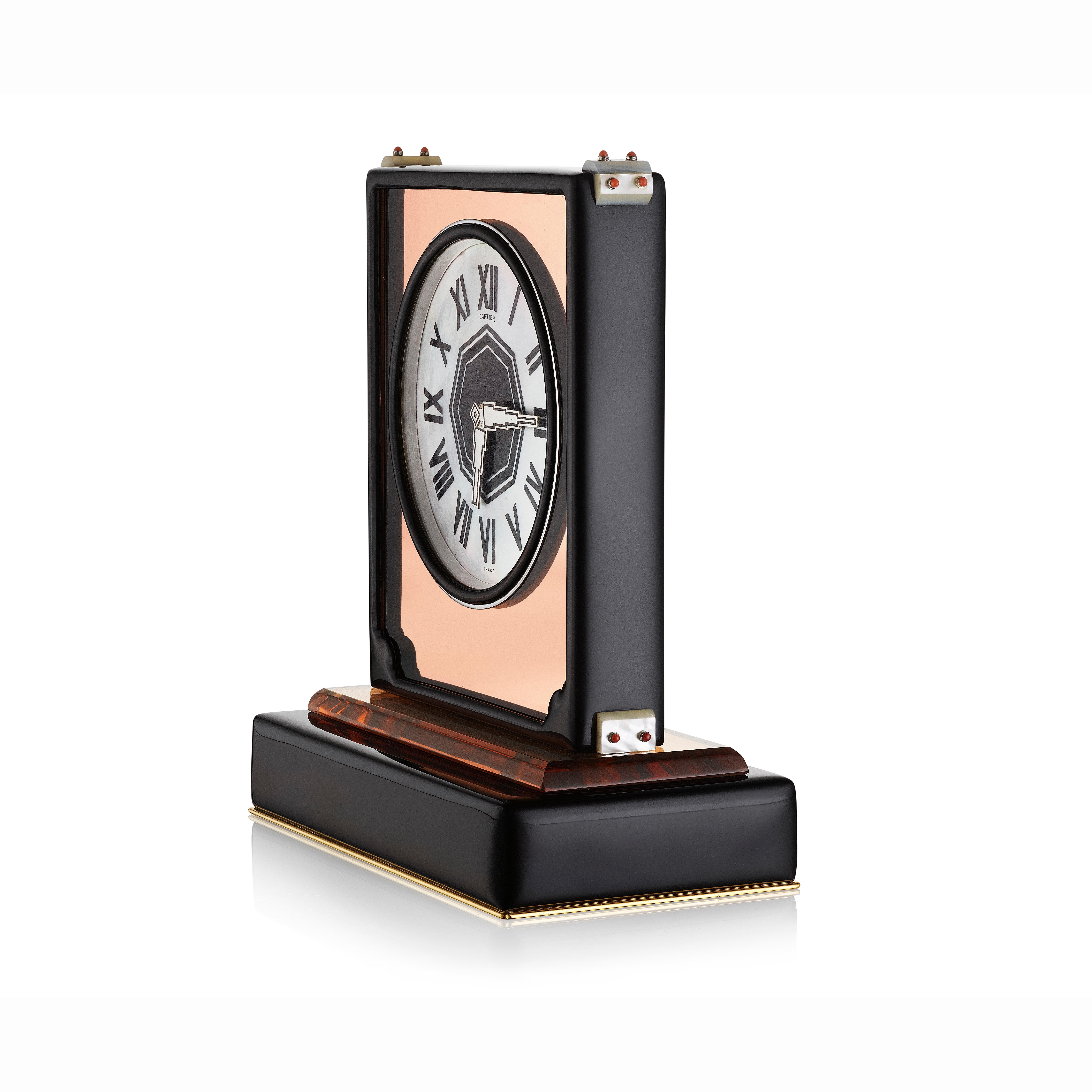 A desk clock composed of a circular mother-of-pearl dial with black enamel Roman numerals set into a rose mirrored rectangular case with black enamel frame, the corners decorated with mother of pearl and coral beads, on a rock crystal and enamel