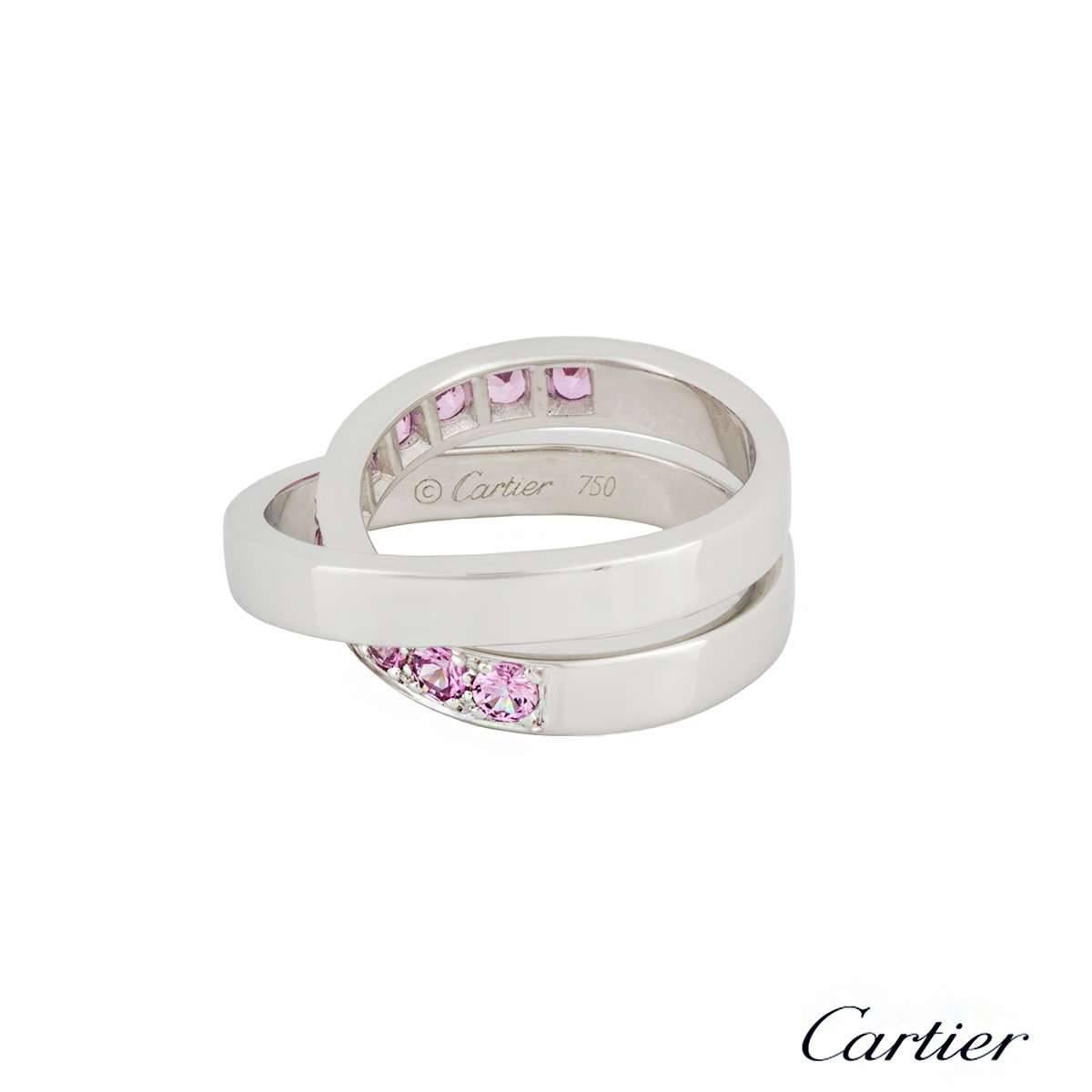 A Cartier Paris Nouvelle Vague pink sapphire ring in 18k white gold. The ring is made up of a cross over design set with 11 pave set round brilliant cut pink sapphires on the preliminary band. The ring measures 8mm wide, is a US size 4 3/4, EU size