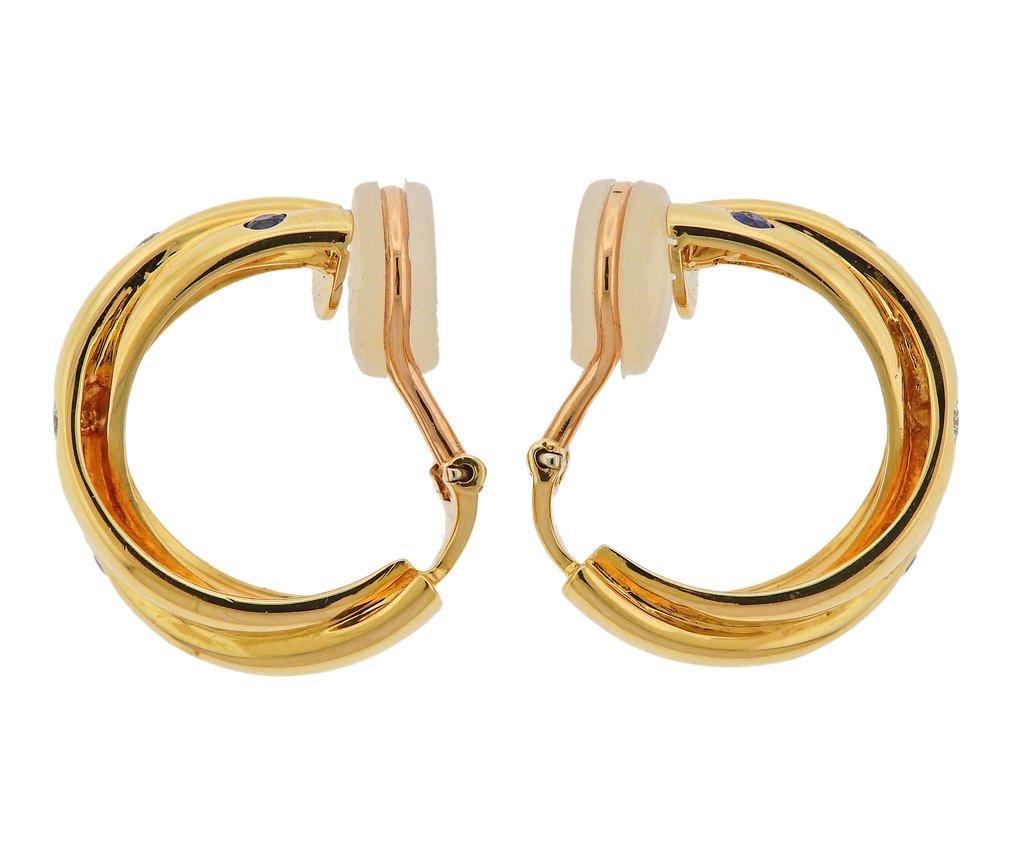 Pair of 18k yellow gold Trinity hoop earrings by Cartier Paris. Set with approx. 0.12ctw in diamonds, sapphires and rubies. Earrings are 22mm in diameter x 6.5mm wide. Weight is 14.9 grams. Marked Cartier, F27 159, 750, 1995, French mark.