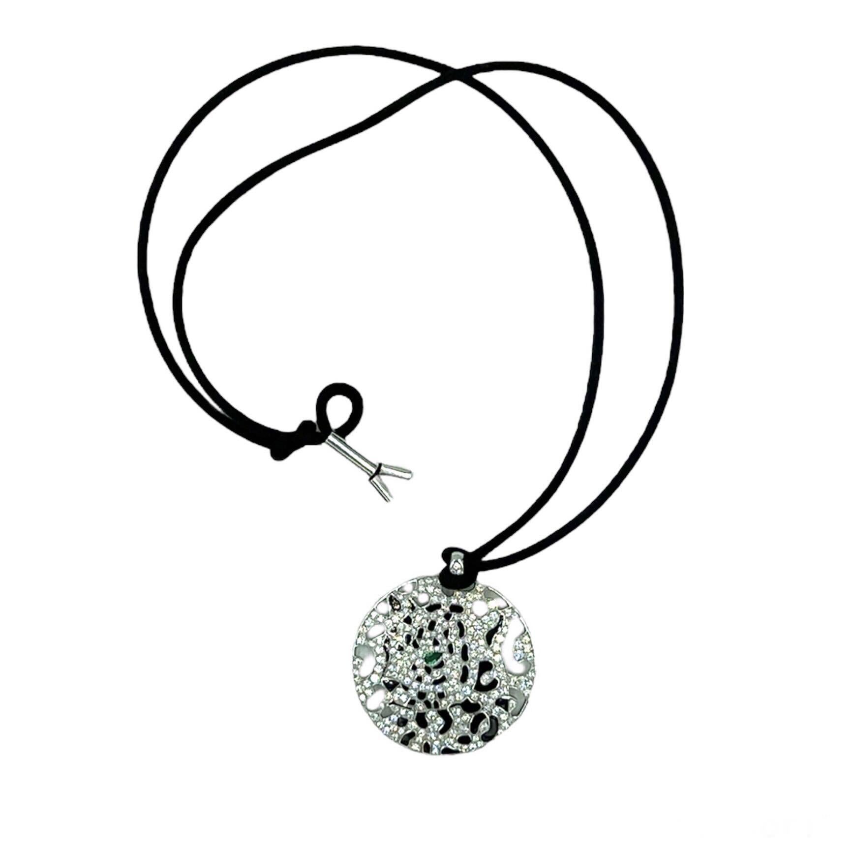 An 18 karat white gold, diamond, enamel, emerald and silk cord necklace, Cartier.  The “Panthere” disc pendant of openwork white gold with pave diamonds, black enamel spots and a pear shaped emerald eye measuring approximately 3.15 x 2.32 mm. on a