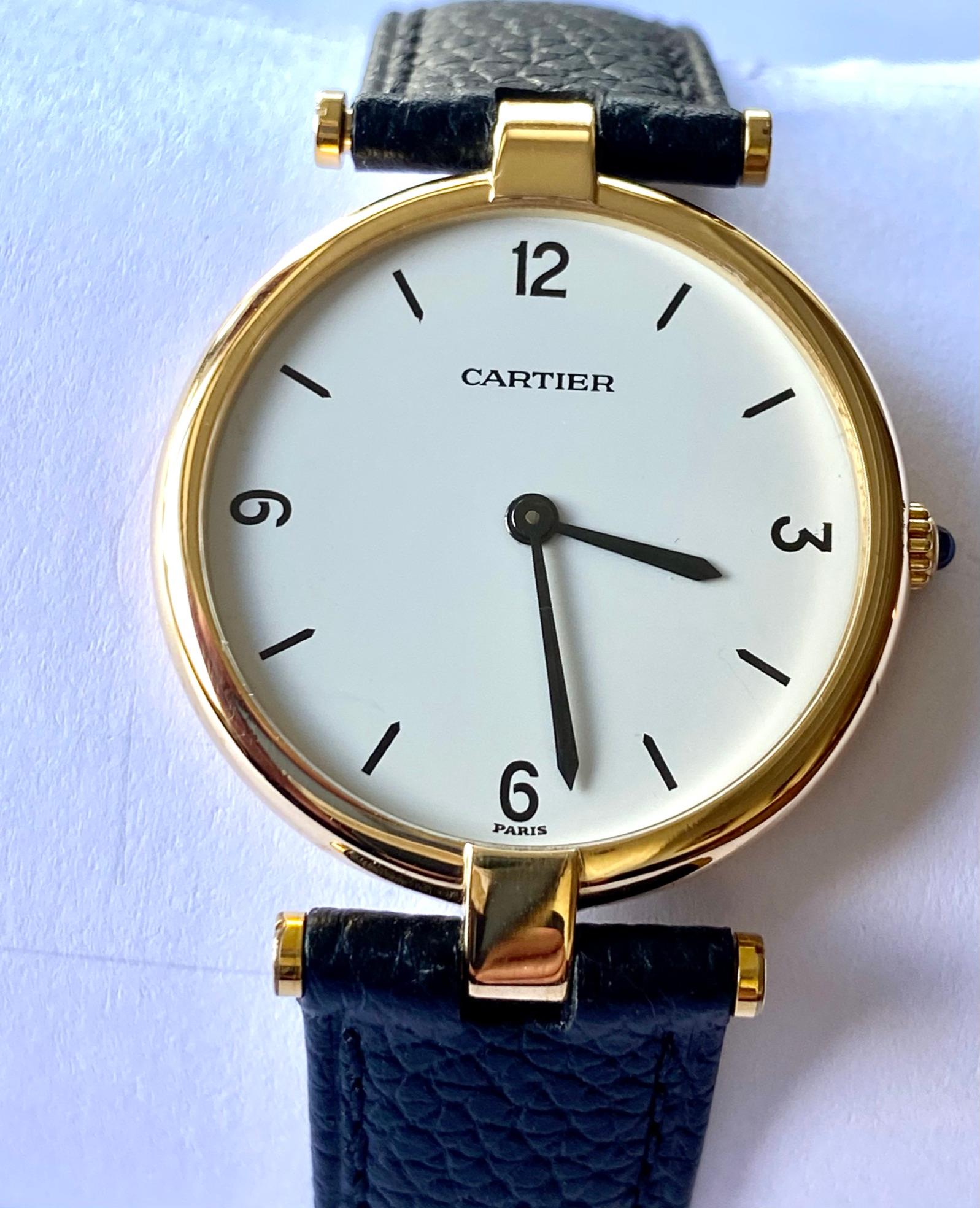 Eine (1) 18K. Gelbgolduhr mit Lederarmband.
Marke: Cartier  Paris  hergestellt ca. 1975
Modell: Großes Vendôme (VLC)  Nr. 81001
Besonderes Zifferblatt: weiß und arabische Zahlen 12  3   6   9
Schwarzes Lederband mit doppelter Buccle.

