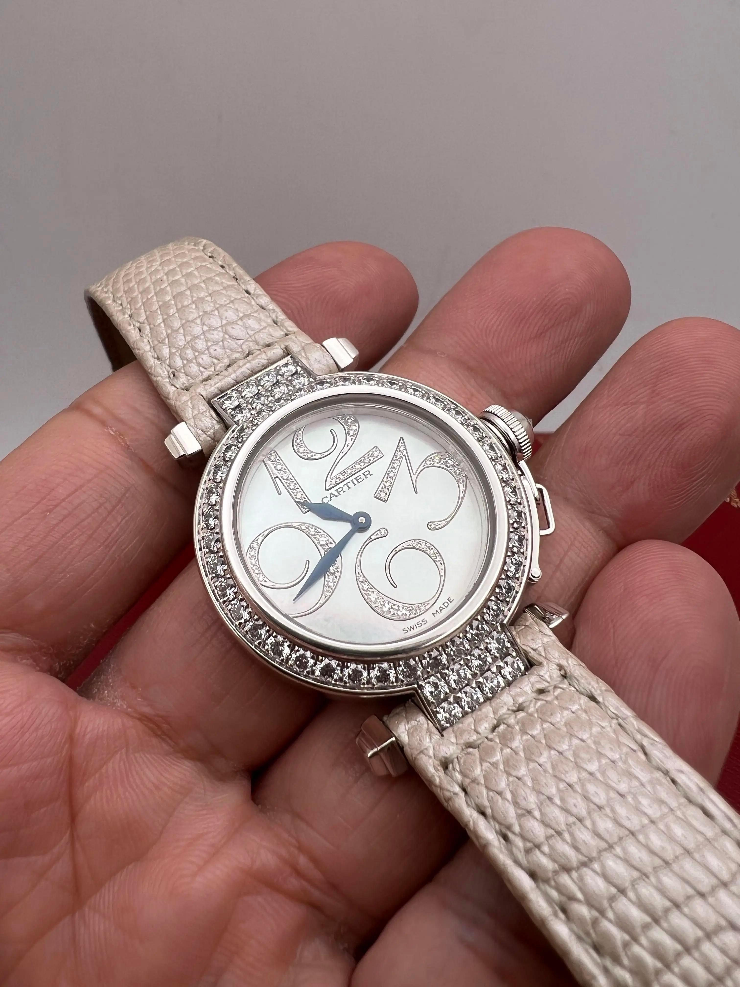 La Cartier Pasha 32mm (référence WJ123221) est un garde-temps luxueux qui illustre l'engagement de Cartier en matière d'élégance et de savoir-faire. Fabriqué en or blanc 18 carats, le boîtier rond de 32 mm est orné de diamants sertis en usine sur la