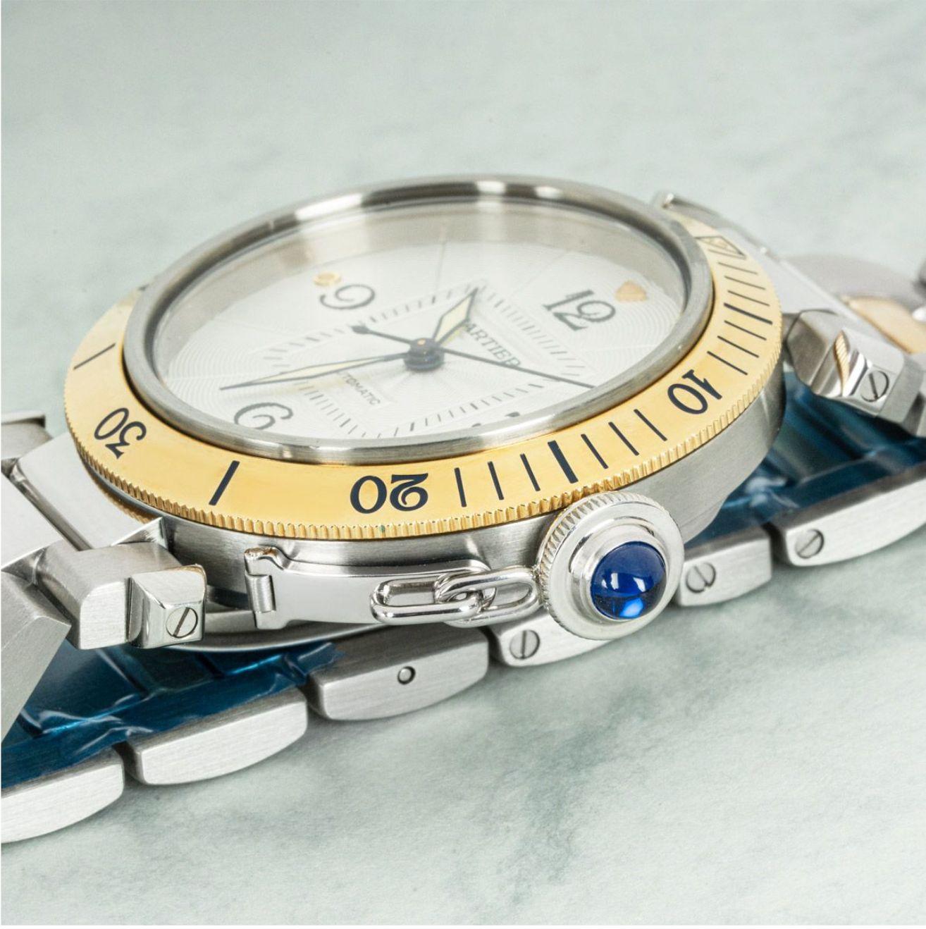 A mens 38mm stainless steel and yellow gold Pasha by Cartier. Featuring a silver guilloche dial with a date aperture and sword-shaped hands in blued steel. The crown is protected by a screw-down cover which is set with a sapphire cabochon.

Equipped