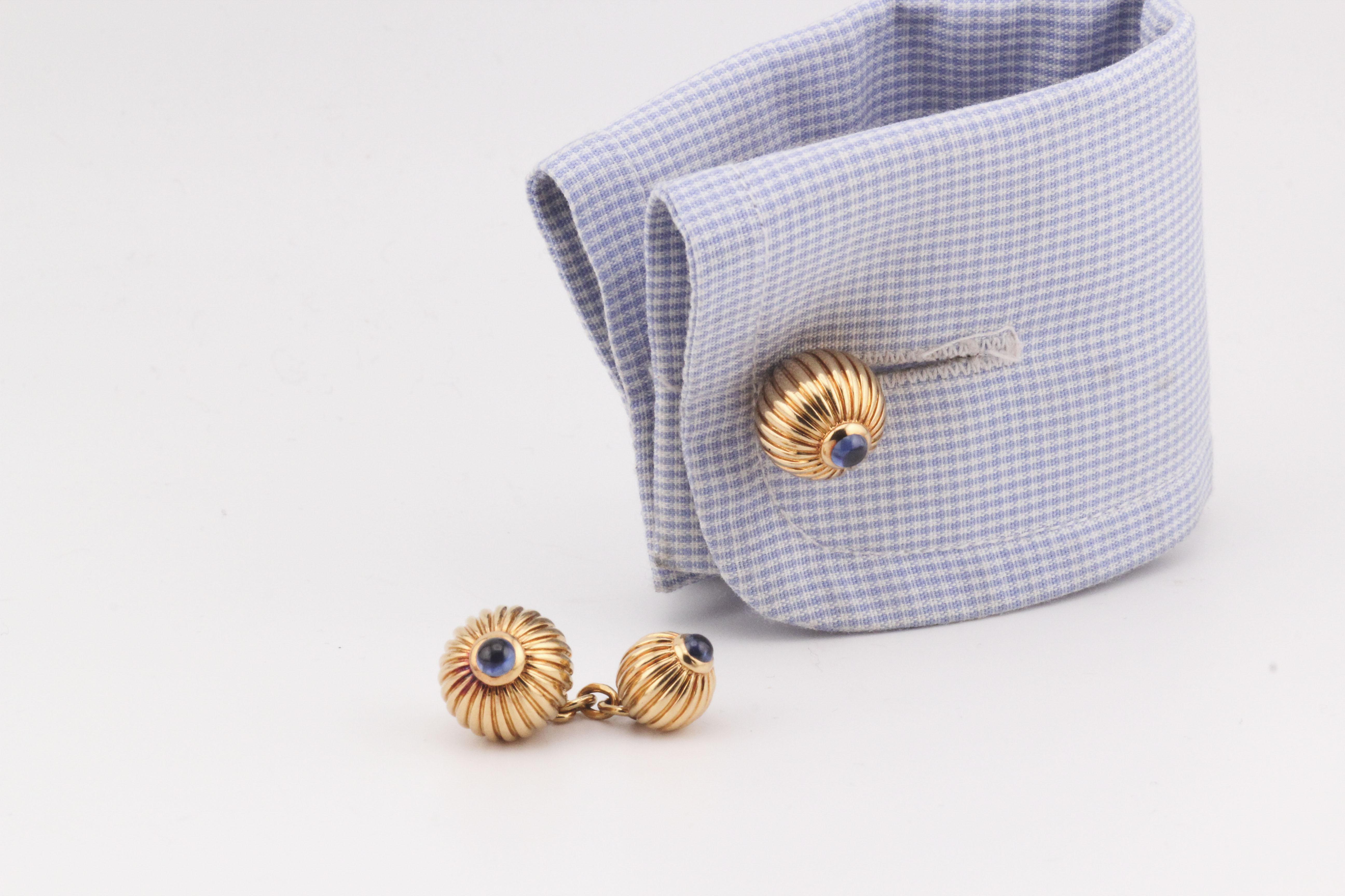 The Cartier 18k Gold Cufflinks are a testament to exquisite craftsmanship and luxurious design. These cufflinks feature a ribbed, spherical form, each adorned with a striking blue sapphire at the center. The sapphire's deep hue contrasts beautifully