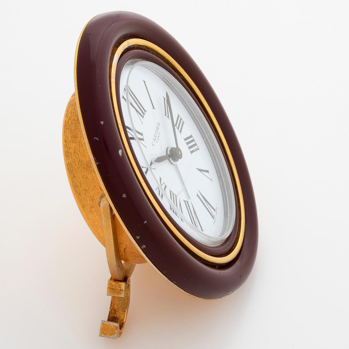 Unser mechanisch aufgezogener Cartier Pendulette-Wecker im Vintage-Stil misst 90 mm x 75 mm. Der Gesamtzustand ist gut, die rote Emaille weist Gebrauchsspuren auf, das Glas hat leichte Abnutzungserscheinungen. Wir datieren die Produktion auf ca.