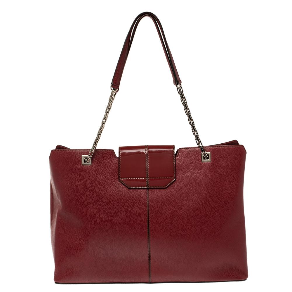 Crafted from red leather and designed with a turn-lock adorned flap, this tote exudes a classic appeal that's true to Cartier’s aesthetics. It is geld by two chain-leather handles and equipped with protective metal feet and a spacious suede