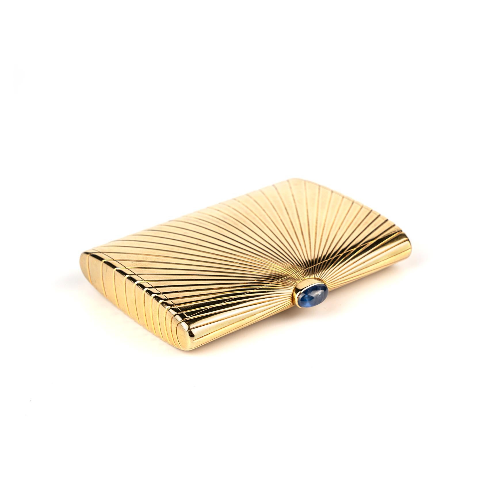 A sumptuous and collectible Cartier Paris golden compact in 18k gold with sapphire clasp, showcasing a sunburst pattern. Made in France, circa 1960.

