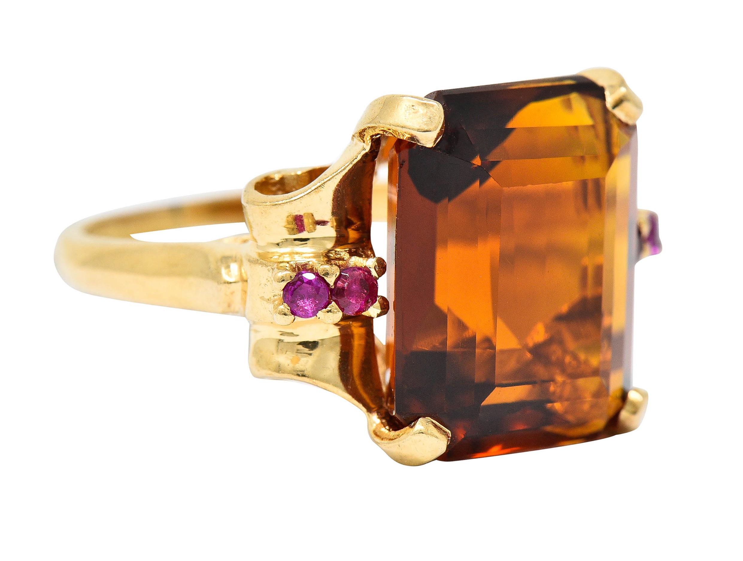 Centering an emerald cut citrine measuring approximately 14.0 x 11.8 mm

Transparent with strong brownish orange color

Set in a stylized basket with scrolled volute shoulders

Accented by round cut rubies - well matched in purplish red