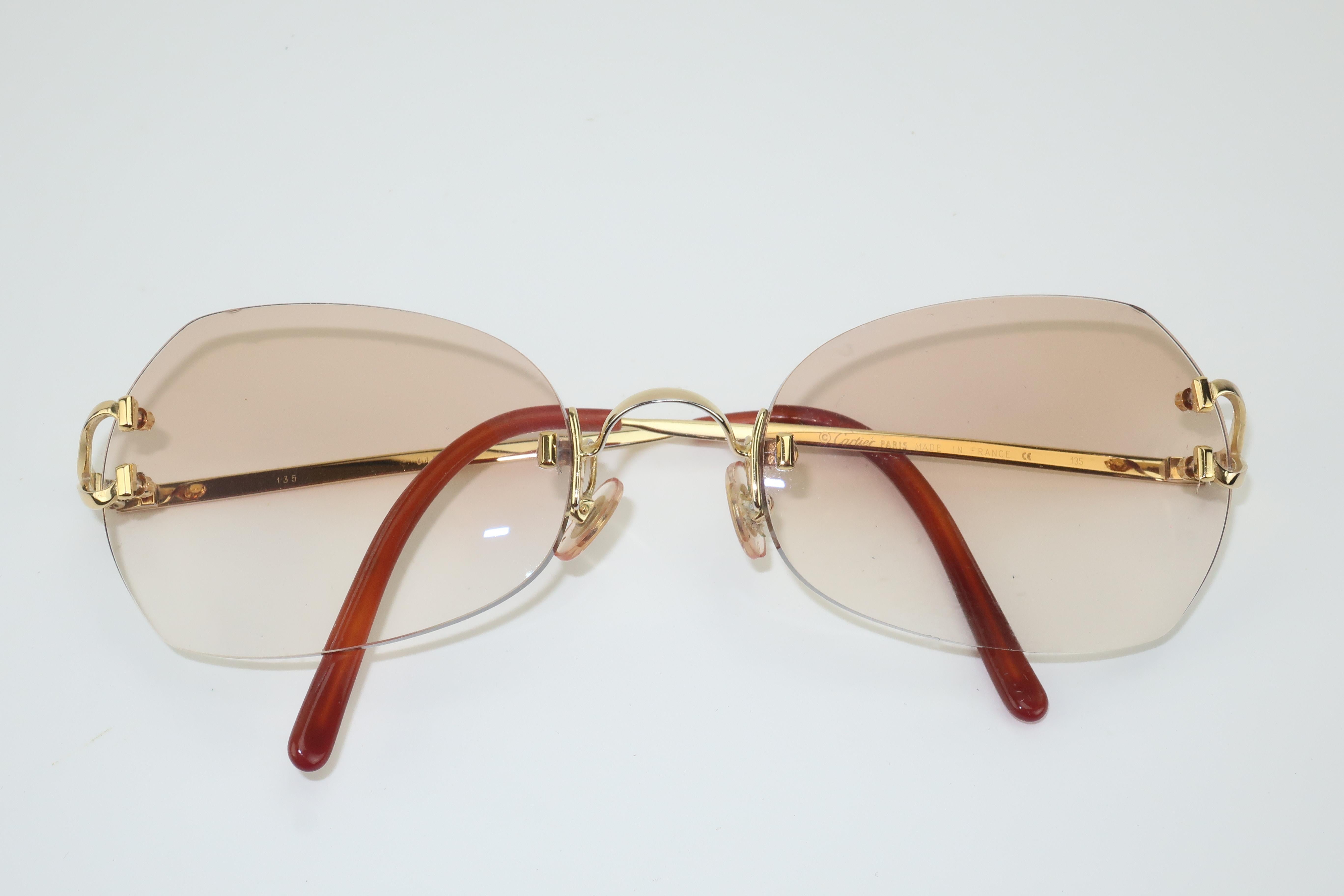 1980’s Cartier rimless sunglasses with a gold finish and gradient amber lenses.  The iconic ‘C’ hinges the lens to the arm which has a faux tortoise ear guard and a Cartier medallion.  The inside of the left arm is hallmarked and the right arm has a