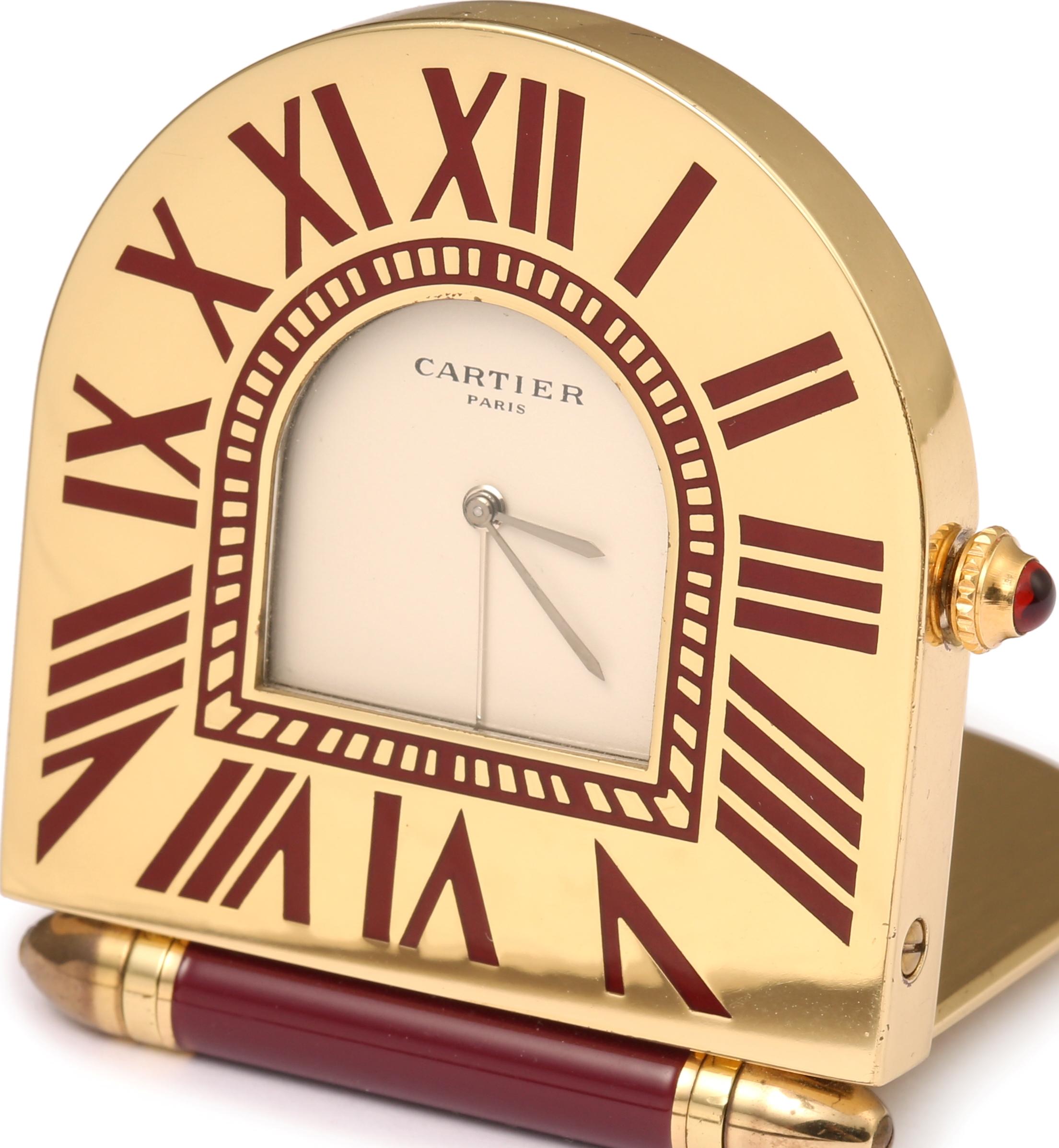 Sublime Cartier travel clock in gilded brass and red lacquer.

Thanks to its articulated plate, it opens to reveal the dial with its red Roman numerals.

The crown stem is set with a red stone.

Dimensions: 6 x 5 x 1 cm (2.362 x 1.969 x 0.394