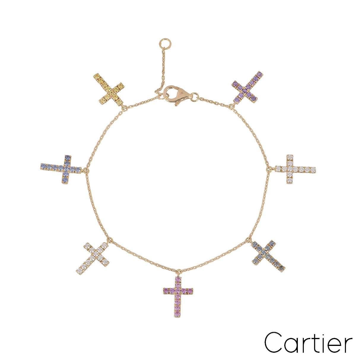 Un elegante bracciale charme in oro rosa 18 carati di Cartier. Con sette motivi a croce ornati da diamanti e una serie di zaffiri nelle tonalità del rosa, giallo, blu, viola e verde. Il pezzo è incastonato con 22 diamanti rotondi a taglio brillante