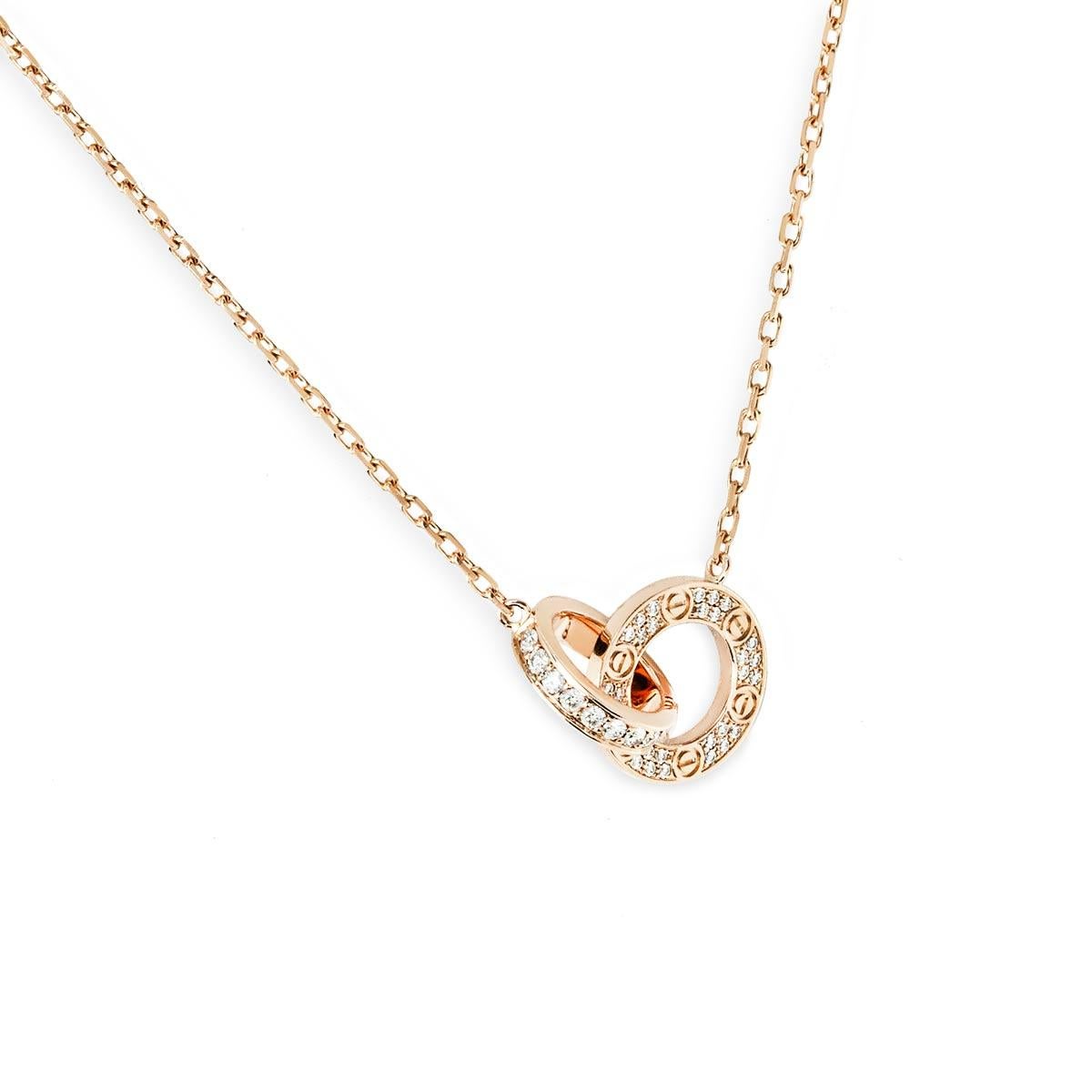 A beautiful 18k rose gold pendant by Cartier from their iconic Love collection. The necklace features two interlocking circular motifs, displaying the iconic screw motif and both pave diamond set with 48 round brilliant cut diamonds, totalling