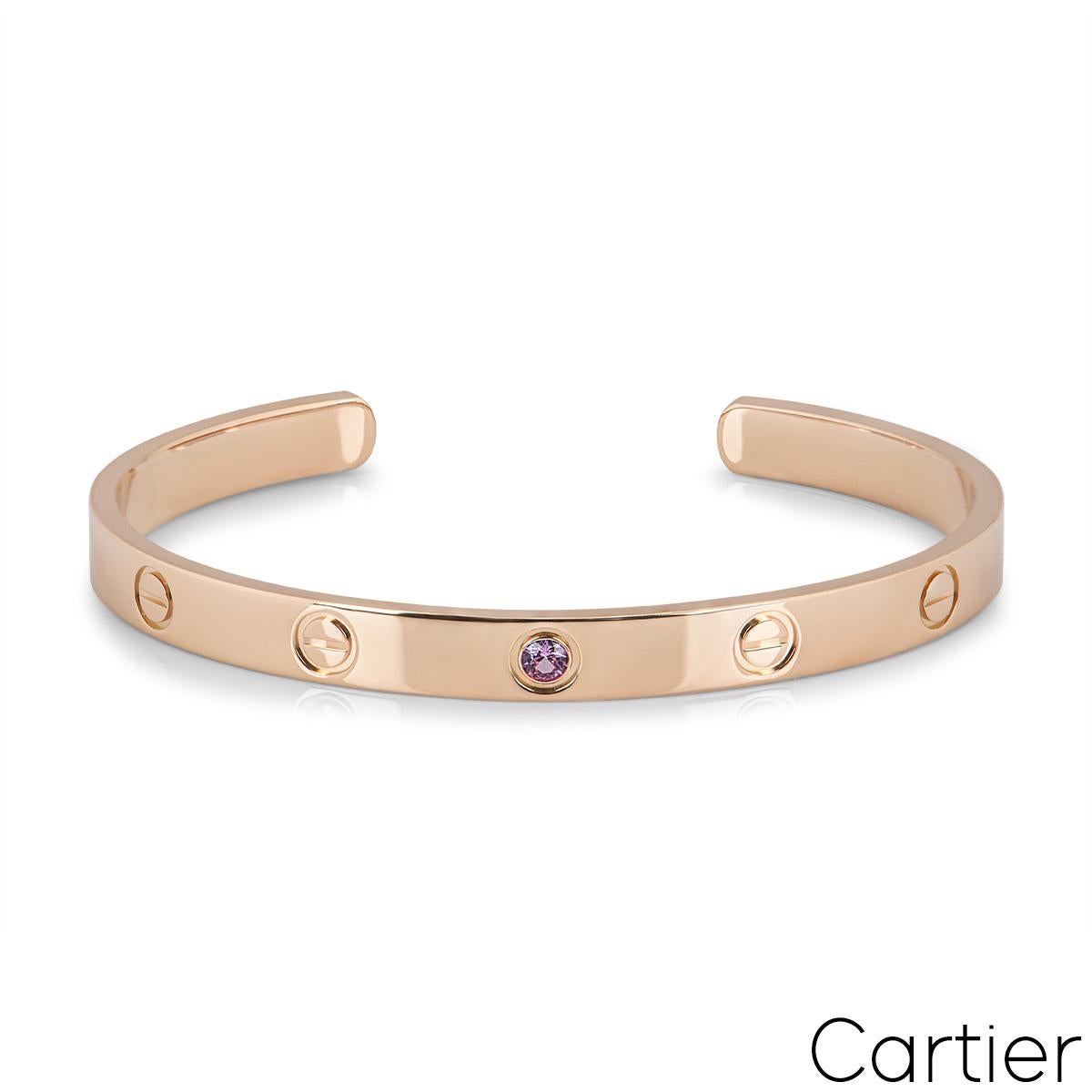 An 18k rose gold cuff bracelet by Cartier from the iconic Love collection. This cuff bracelet has the iconic screw motif displayed throughout with a single pink sapphire in the centre. The bracelet is a size 19 and has a gross weight of 28.1 grams.
