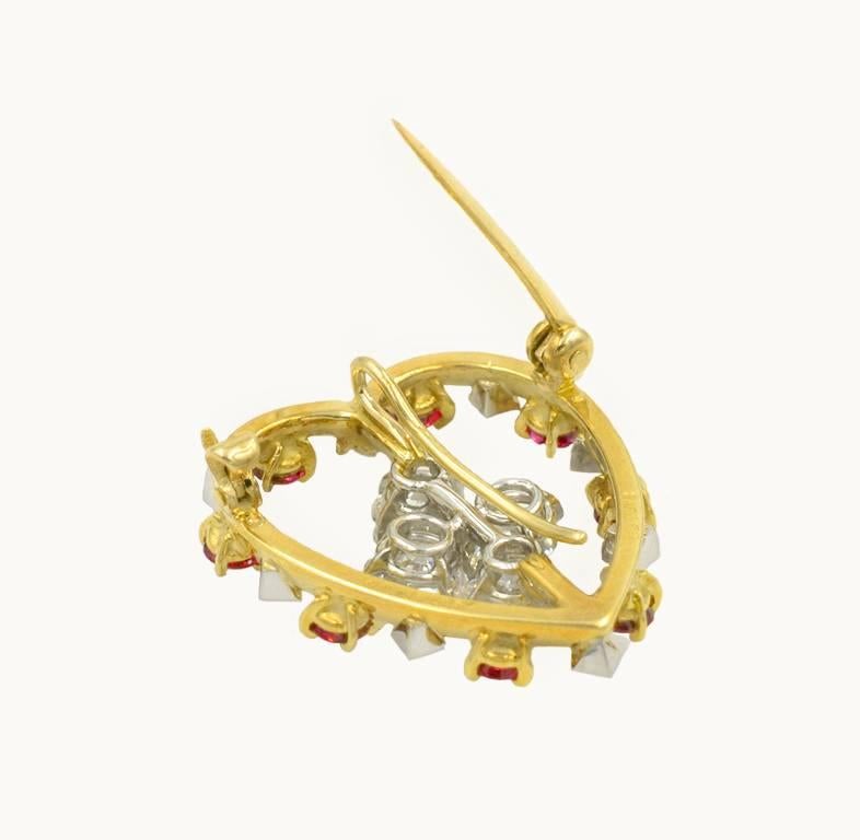 Cartier ruby and diamond heart brooch in 18 karat yellow gold and platinum from circa 2000s.  This brooch features alternating 8 round rubies with 8 round diamonds set in a heart shaped outline.  The center of the brooch features four round