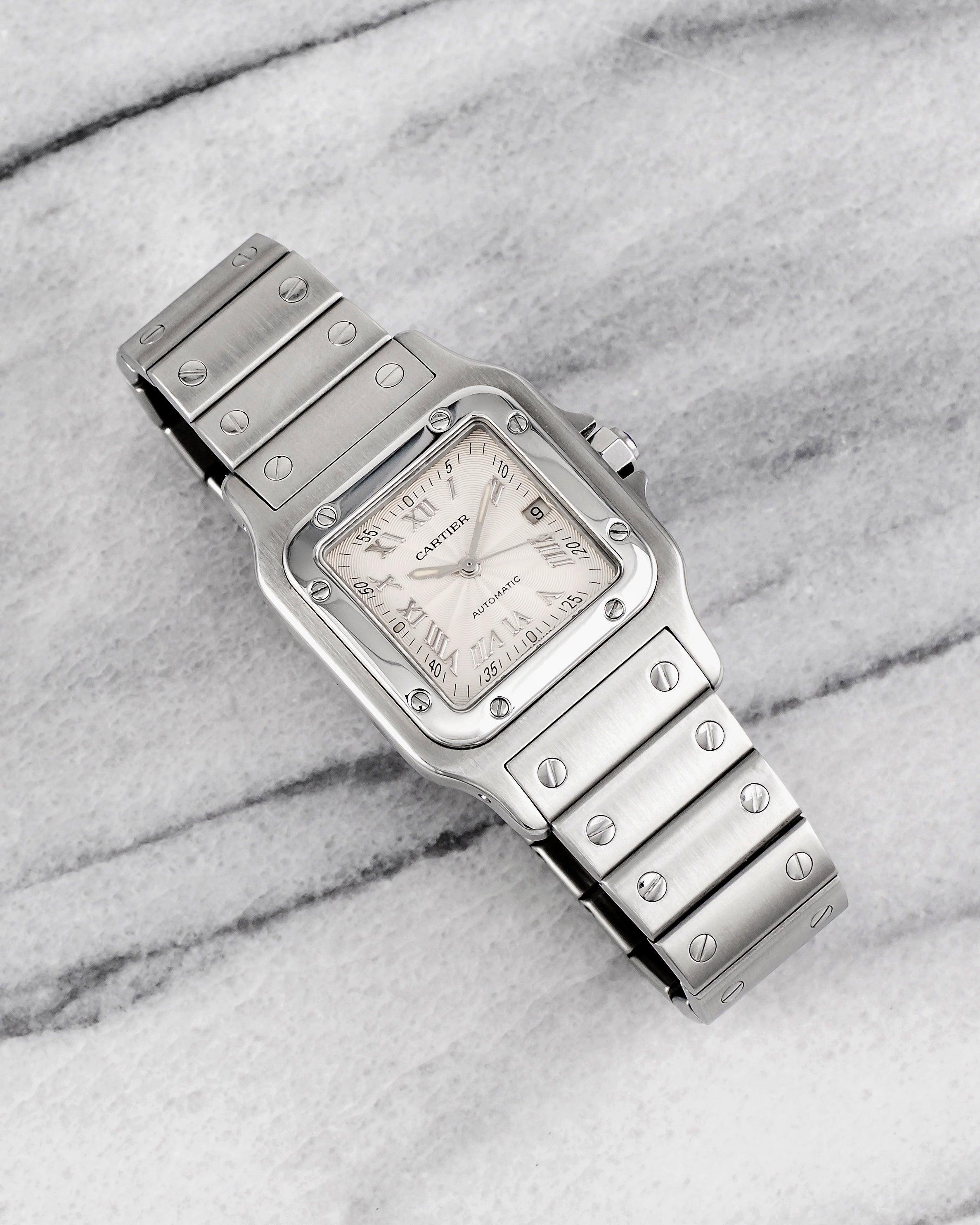 Aquí tienes un Cartier Santos vintage referencia 2319 automático con esfera guilloché y brazalete de acero de los años 90. Mantiene la hora y es totalmente funcional. Las medidas incluyen una caja de acero de 29x41 mm y una anchura de orejetas de 18