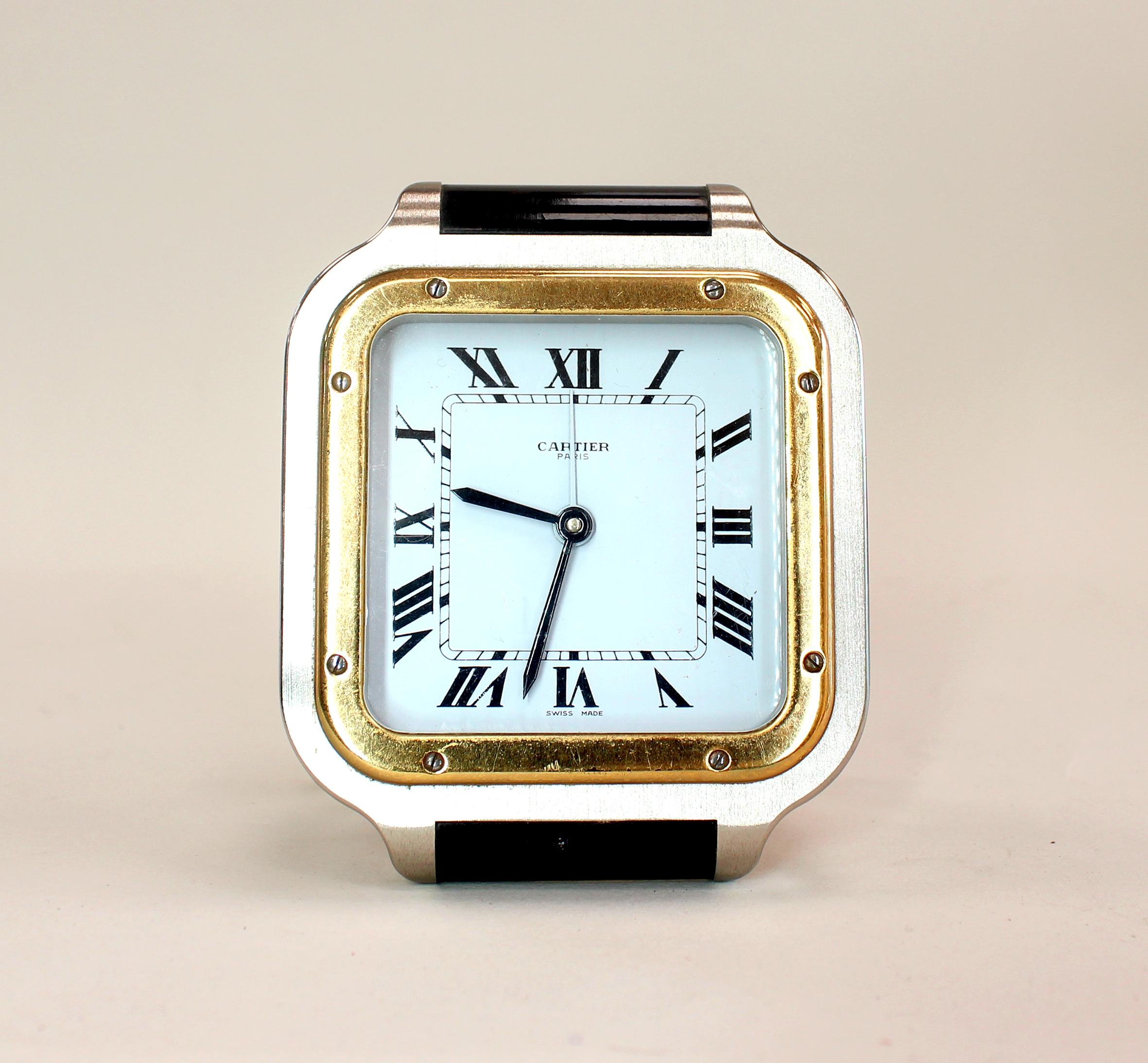 Ein Cartier-Tischwecker in Form der kultigen Santos de Cartier Uhr. Mit goldener Lünette, gebürstetem Stahlgehäuse und schwarzem Emaille-Detail. Der vergoldete Boden beherbergt ein Schweizer Quarzwerk mit einer Mutter im Cabochon-Schliff, gestempelt