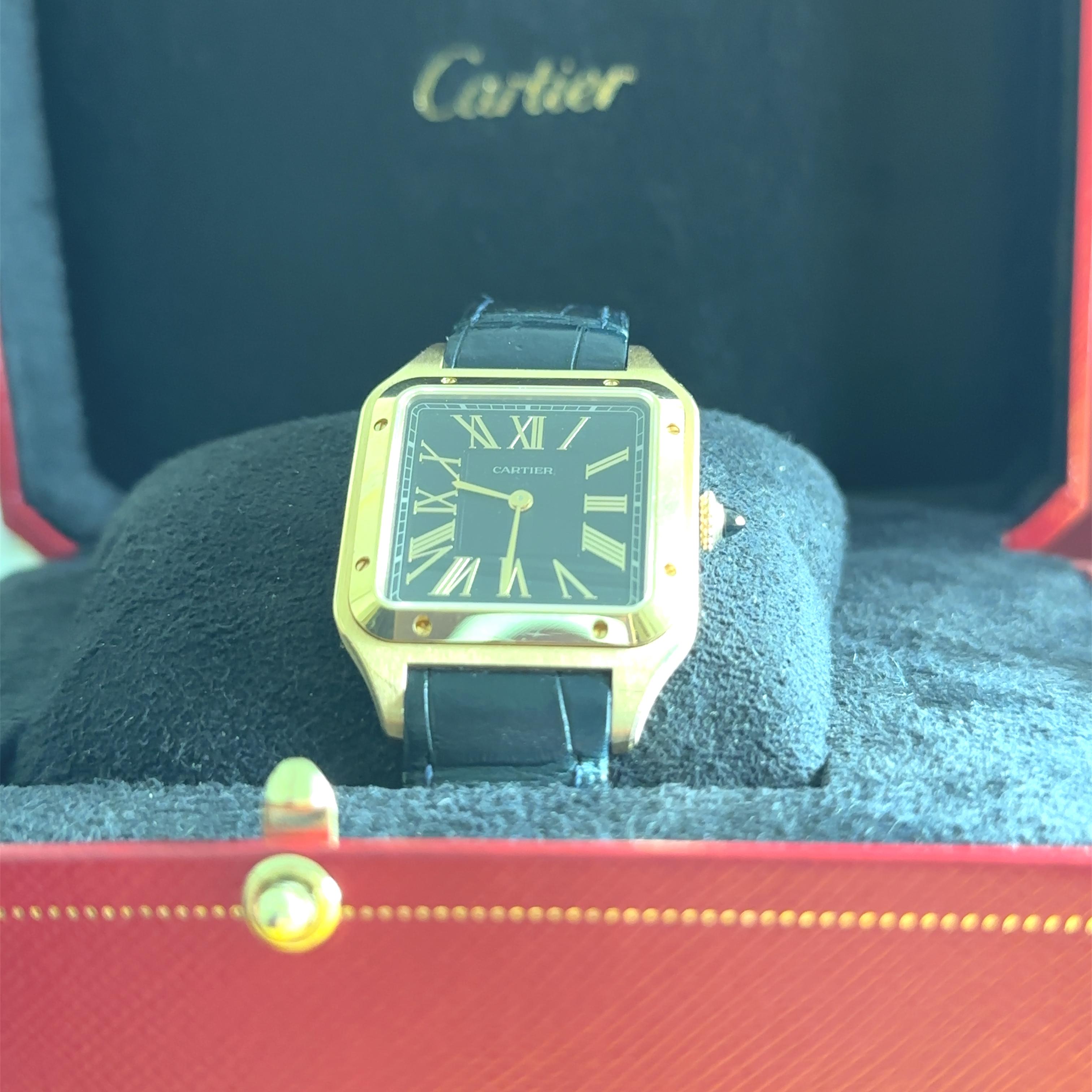A Cartier Santos Dumont Large Model 18ct Yellow Gold Wrist Watch on a black leather strap.

Quartz movement, black dial.

Applied gold Roman numeral markers.

Ref: WGSA0077

Serial: 4532106489DY, circa 2023

Metal: 18ct Yellow Gold 
Carat: