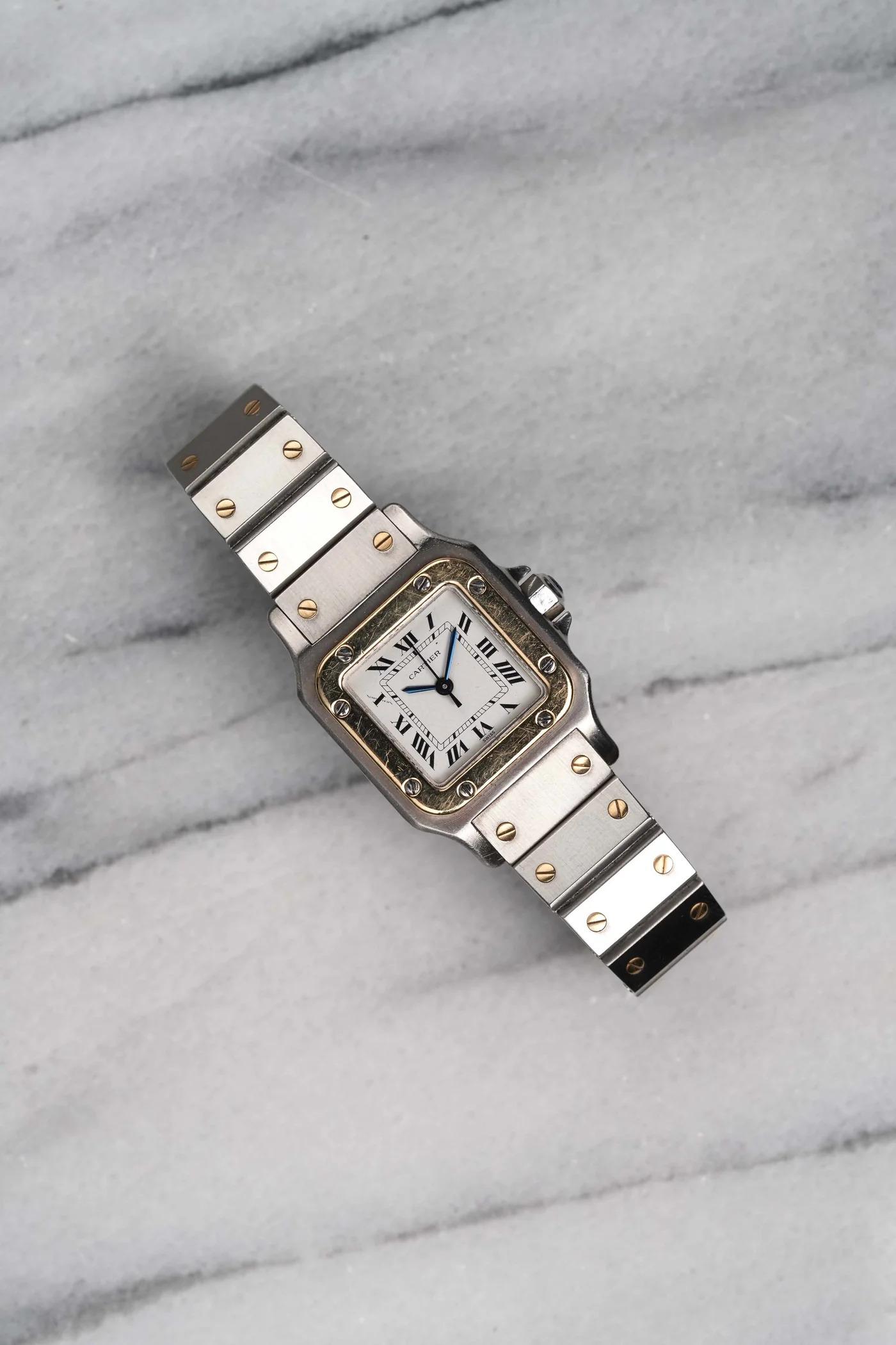 Aquí tienes una Cartier Santos automática bicolor vintage con esfera blanca de números romanos de finales de los 80, principios de los 90. Mantiene la hora y es totalmente funcional. Las medidas incluyen una caja cuadrada de 24 mm y un ancho de asa