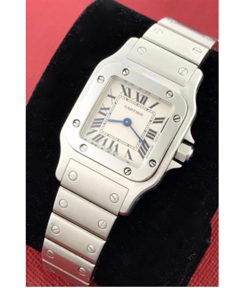 Charming and timeless. This beautiful Cartier Santos is in gorgeous condition. This watch features stainless steel construction. The dial is a silver textured dial that features black Roman numerals. The crown is topped with a blue sapphire