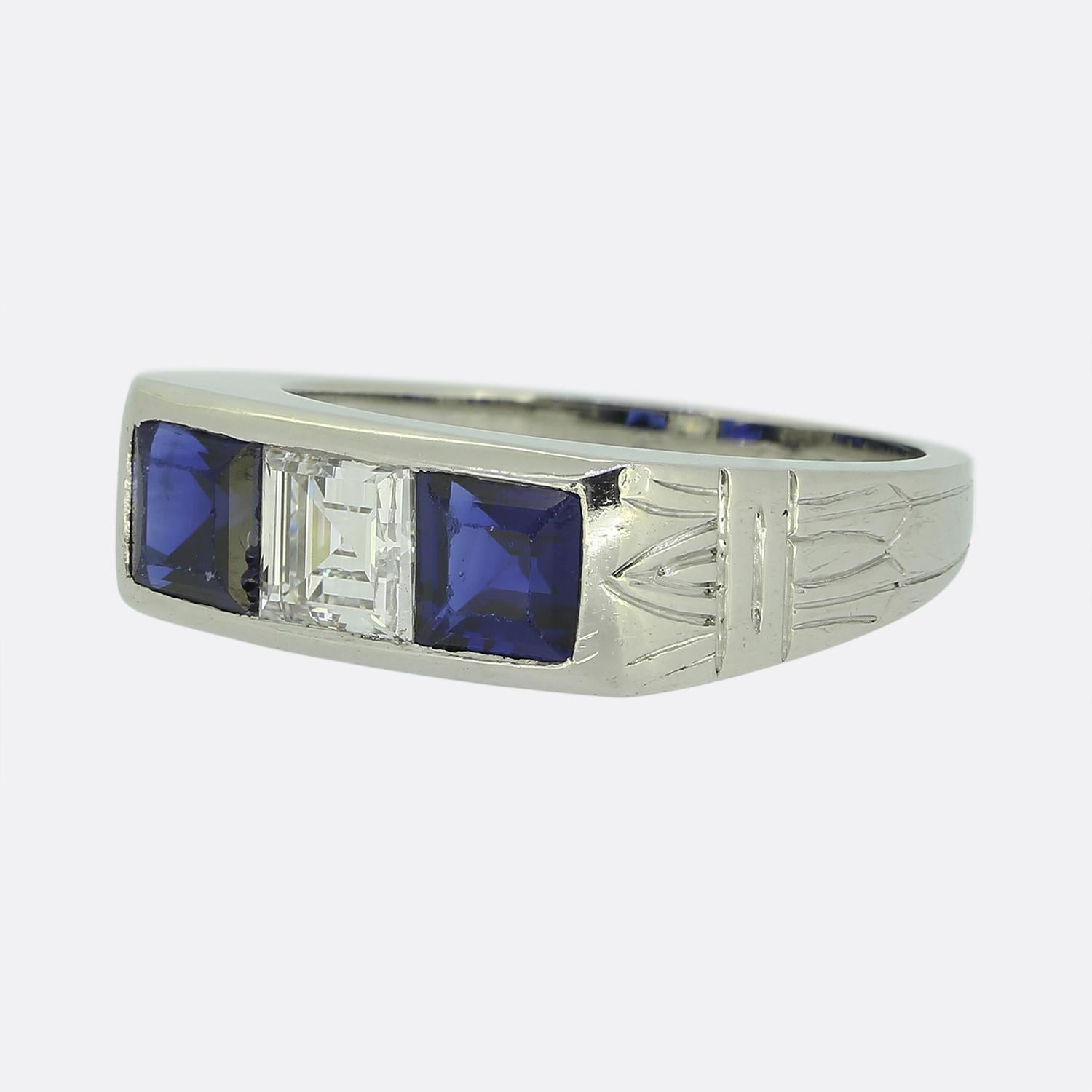 Here we have a refined three-stone ring from the world renowned luxury jewellery house of Cartier. This platinum piece features a centralised square-cut white diamond, flanked by two deep navy blue square-cut sapphires. The design is clean and