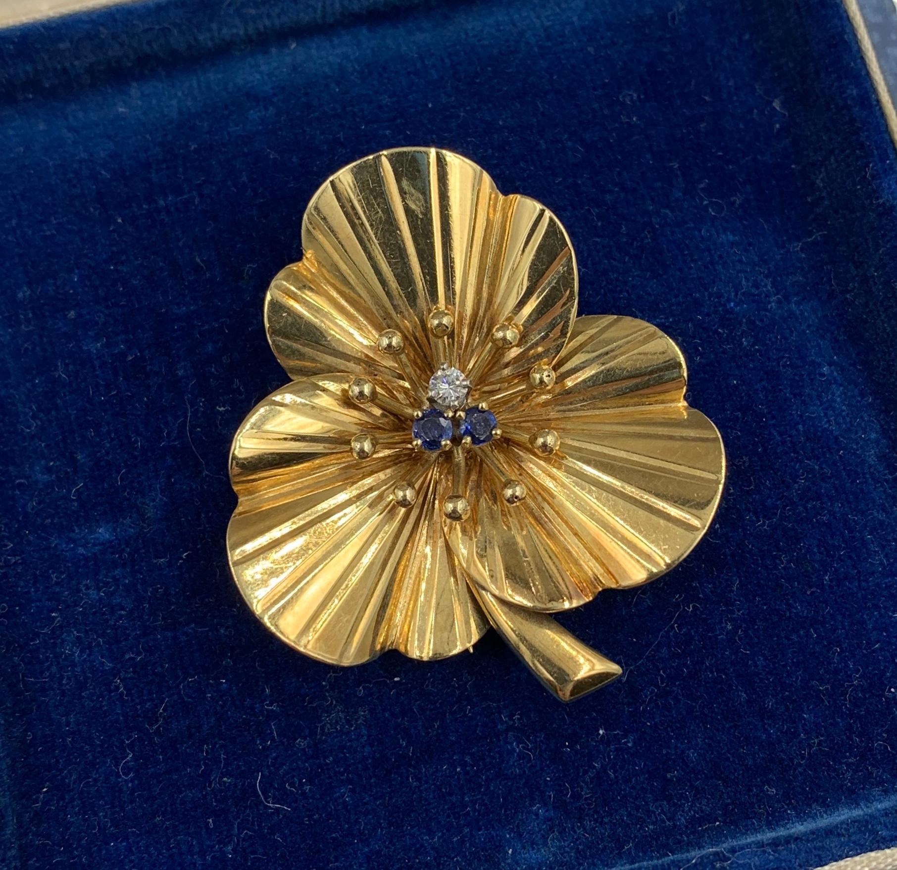 This is a gorgeous and rare Cartier Gold, Sapphire and Diamond Clover Flower Clip Brooch.  The stunning jewel is an Antique brooch by Cartier dating to circa 1950.  The rare clover motif jewel is 14 Karat Yellow Gold.  It has three three-dimensional