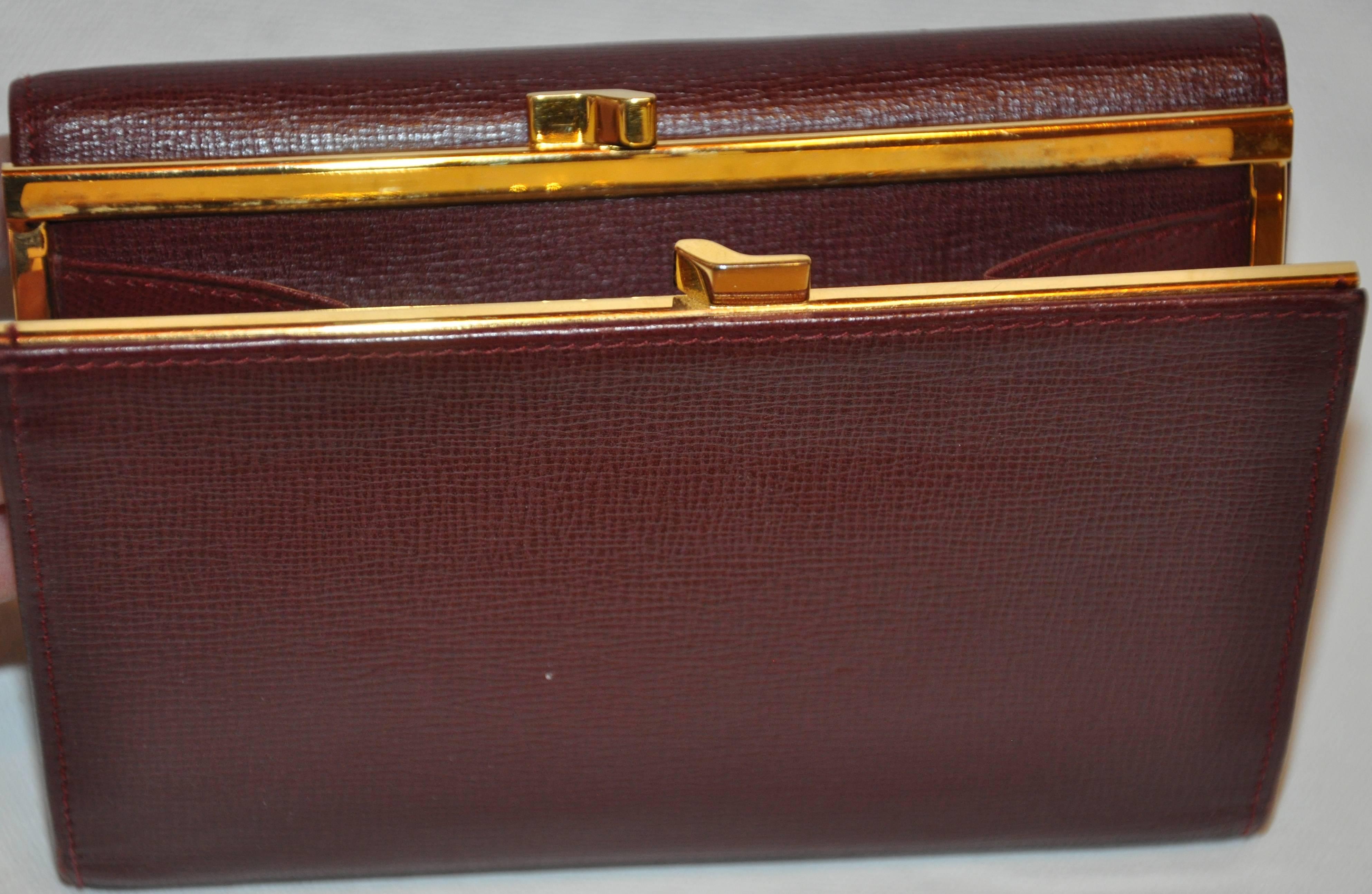 Cartier Signature burgundy textured calfskin wallet offering a billfold, credit card as well as an exterior change purse, accented with gold-tone hardware along the corners and snap-closure. Made in France, when closed, the measurements are 6 inches