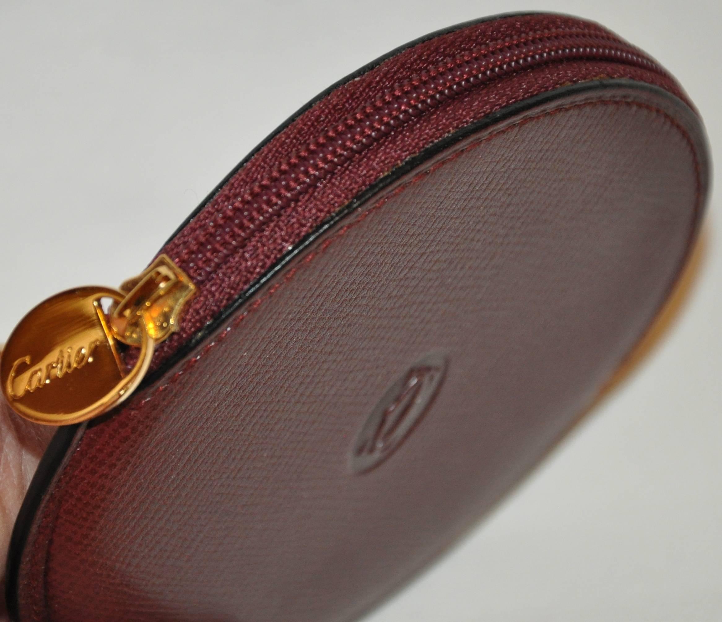        Cartier signature burgundy textured calfskin zippered top change purse, is accented with gold-tone hardware with their signature embossed logo at the center. The change purse measures 3 1/4 inches by 4 inches. The circumference measures 12