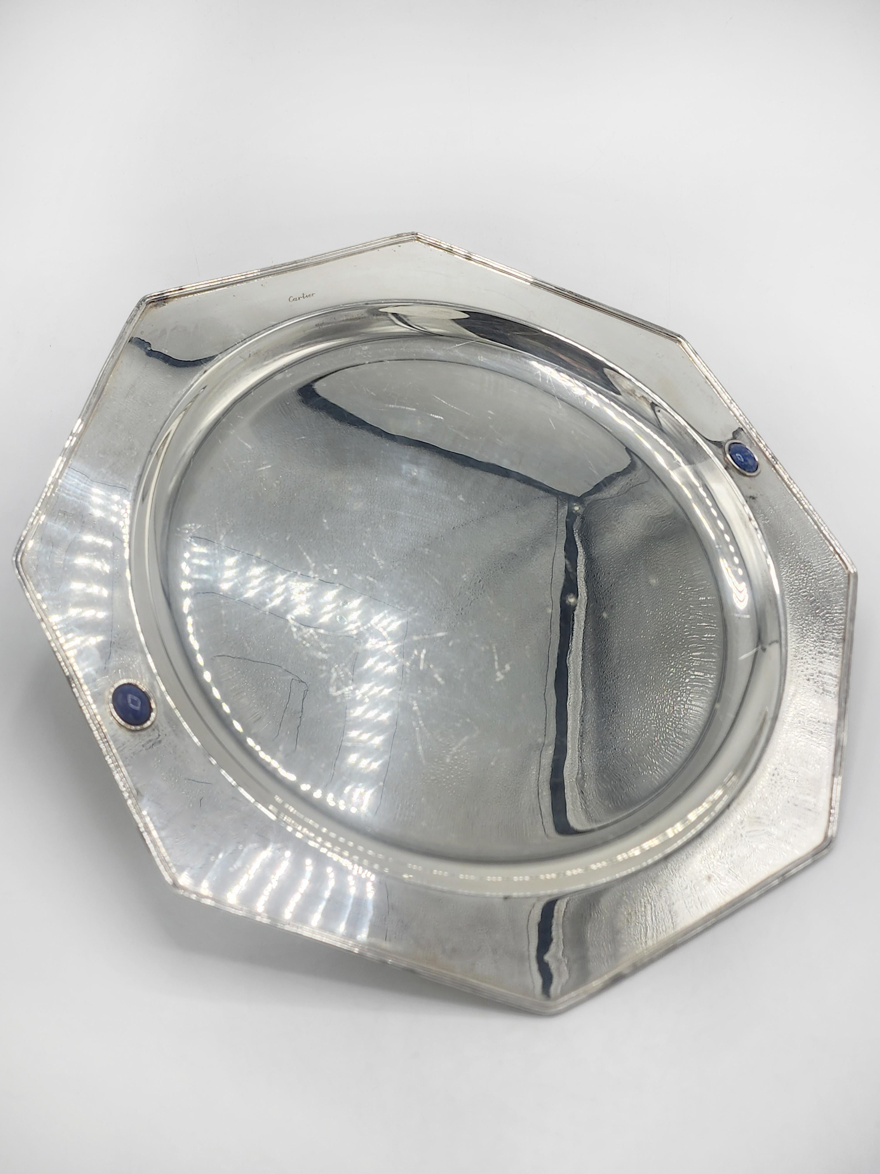 Cartier Silver-Plated Tray
This silver-plated tray from Cartier features an octagonal design with a sunken oval center. Its edges are defined by corners inlaid with round blue lapis lazuli, one on each side. The tray's surface is smooth and
