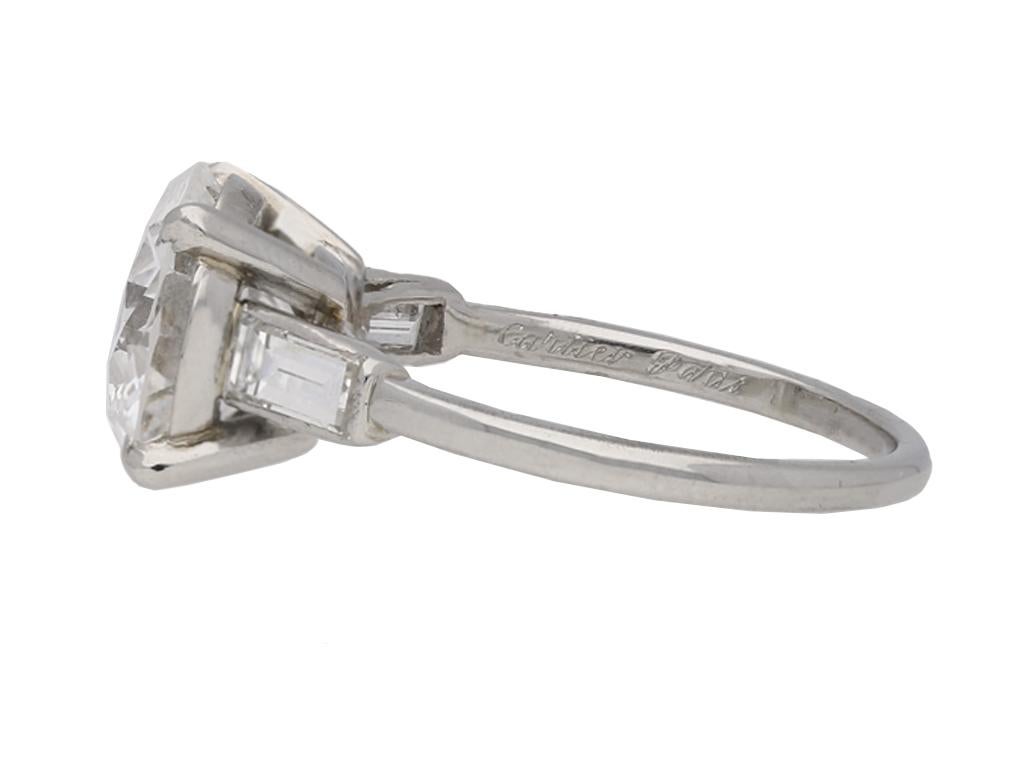 Cartier solitaire diamond engagement ring. Set to centre with a round old cut diamond, D colour, VVS2 clarity, with an approximate weight of 3.27 carats in an open back four claw setting, flanked by two horizontally set rectangular baguette cut