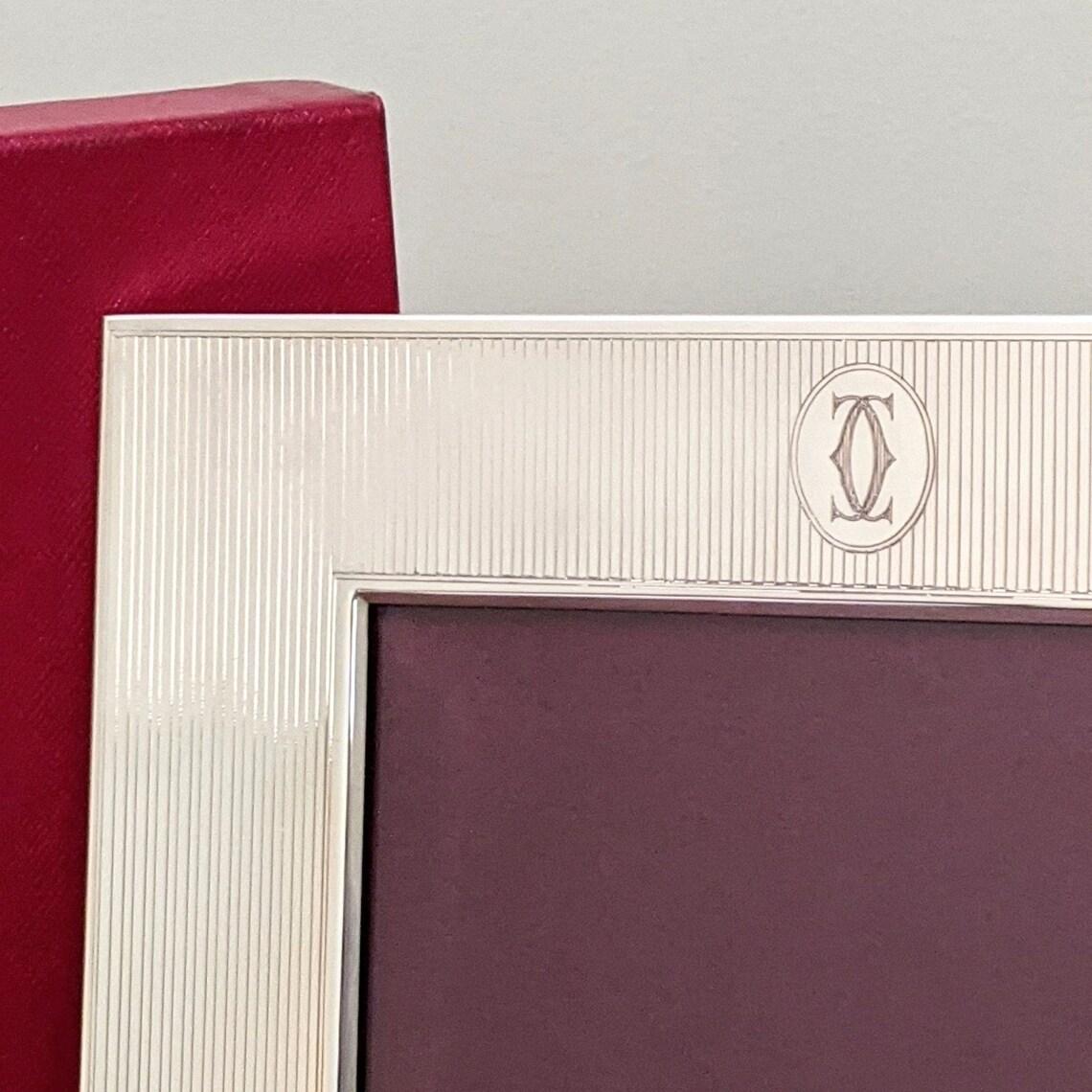 An exquisite Cartier sterling silver and mahogany picture frame. Elegant pin stripe pattern adorned with Cartier's double C logo and a panel that can be engraved. The glass is beveled giving extra depth to the frame. As expected, this is a very well