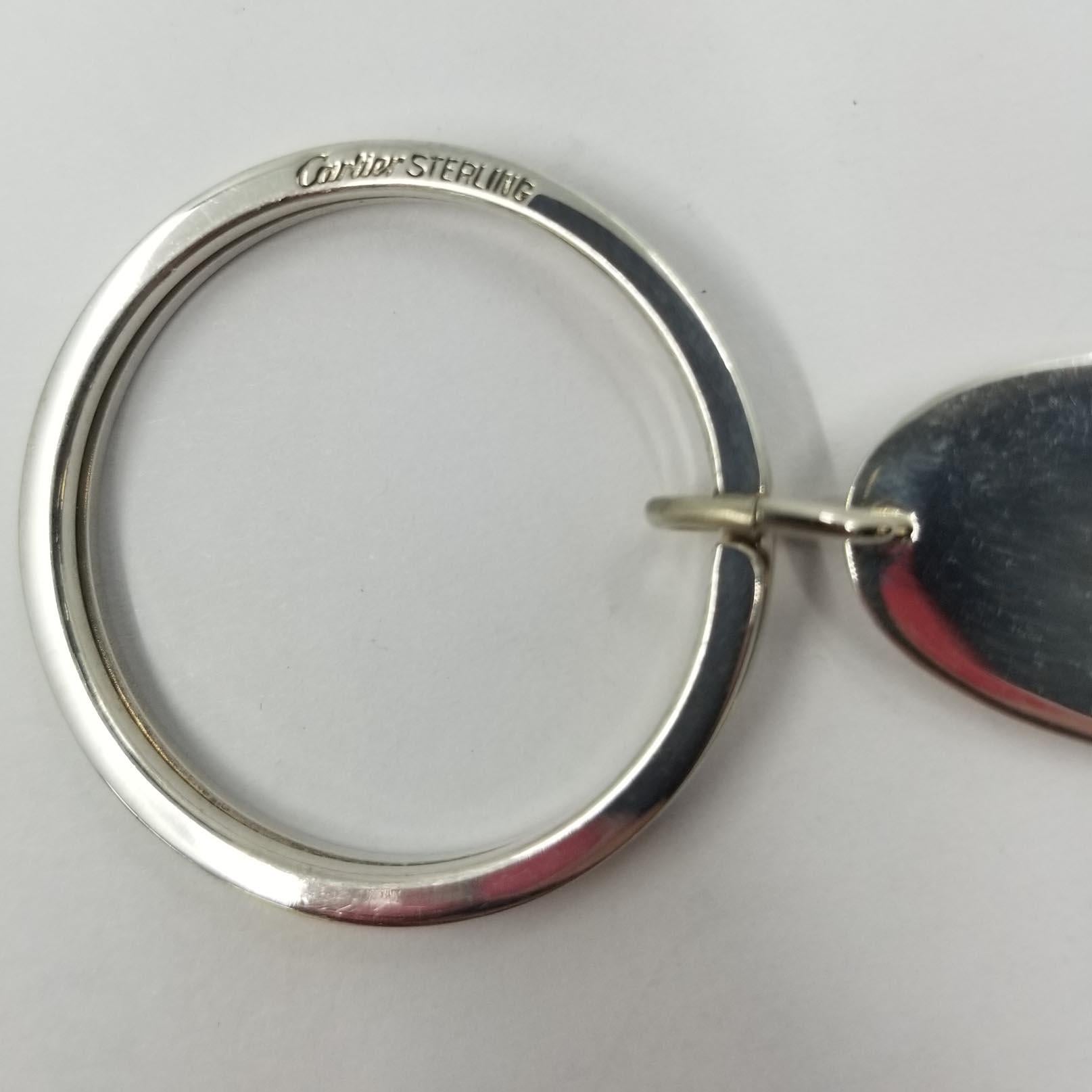 This engravable key ring is designed by Cartier. Both the ring and the flat oval disc charm are sterling silver. The ring is signed Cartier Sterling, and the charm is stamped Sterling. Approximate length is 2.5 inches.
