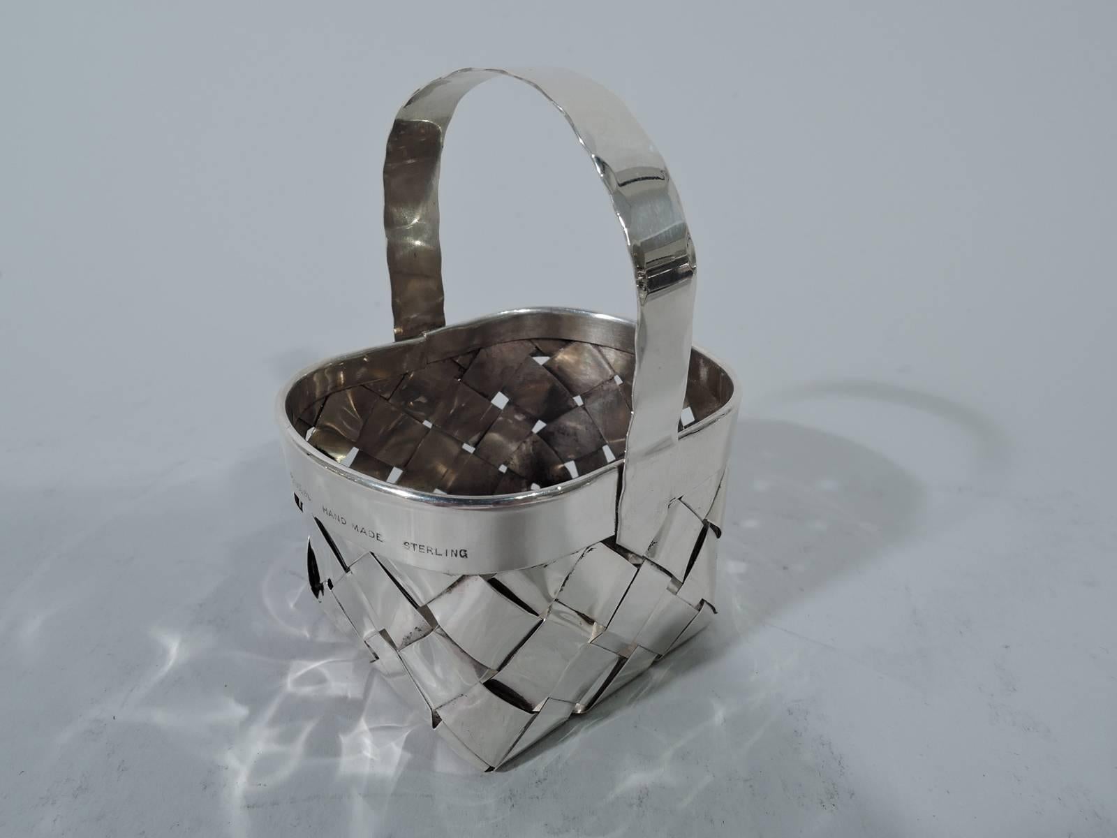 Miniature sterling silver country basket. Retailed by Cartier in New York. Woven sides and bottom, plain rim, and C-scroll handle with faint crimping suggestive of stitching. A witty mix of high and low. Hallmark includes phrase “Hand Made”. Weight: