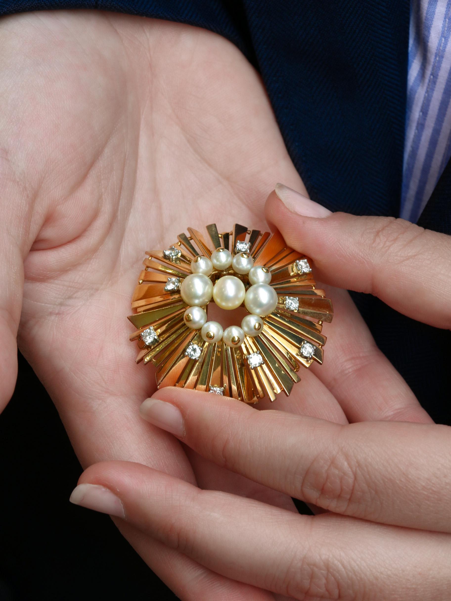 Cartier-Brosche aus 18 Karat Gold (750°/°°), besetzt mit Diamanten und Perlen. 
Die Brosche, die eine Sonne darstellt, besteht aus unterschiedlich großen Strahlen und wird von drei größeren Knopfperlen und vier kleineren Perlen, die von einem