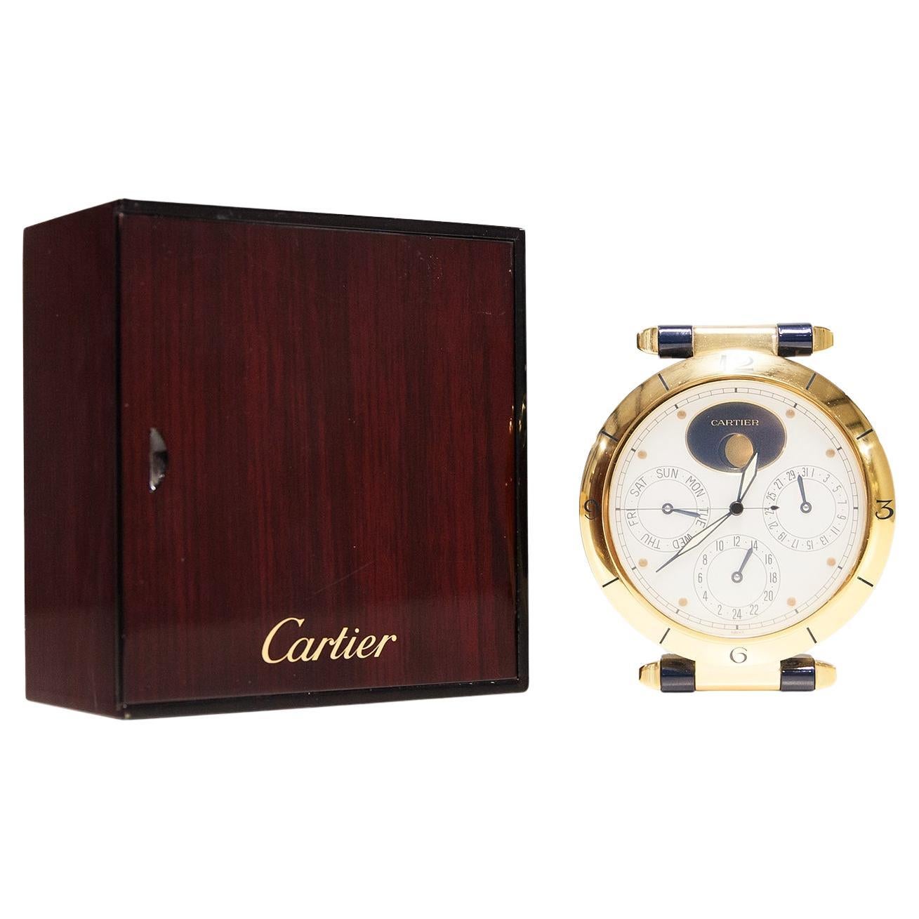 A CARTIER 'PASHA' DUAL TIME ZONE CALENDAR DESK CLOCK WITH MOON PHASE, CIRCA 1995 jewelled quartz movement, frosted silver signed dial with subsidiary dials for the day, date and second time zone below the midnight-blue oval aperture for the moon