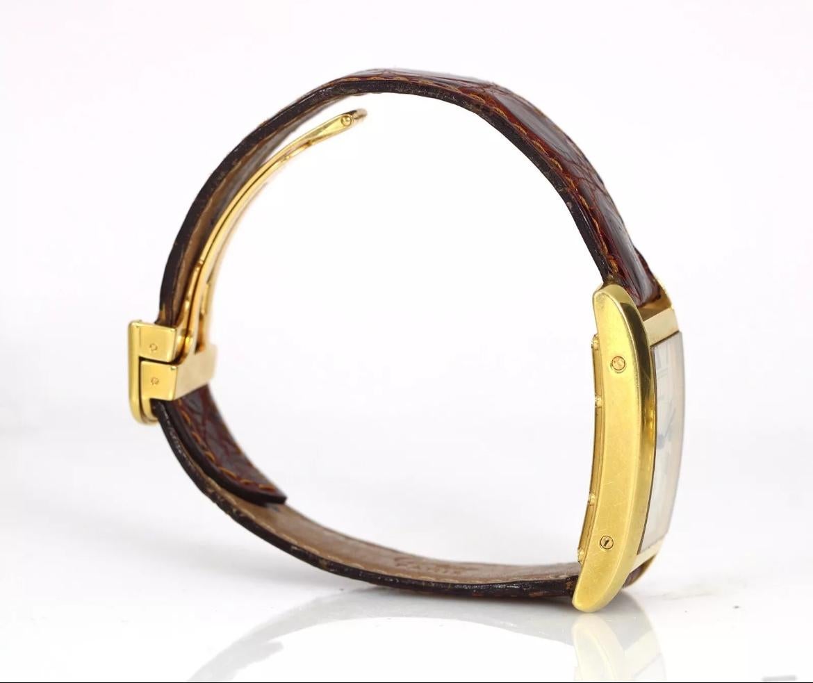 This Cartier Tank Américaine watch is a luxurious accessory suitable for both men and women. The watch features a white dial with brown alligator band and a gold case. The watch is 23mm x 40mm in size and has a screw case back. The movement is