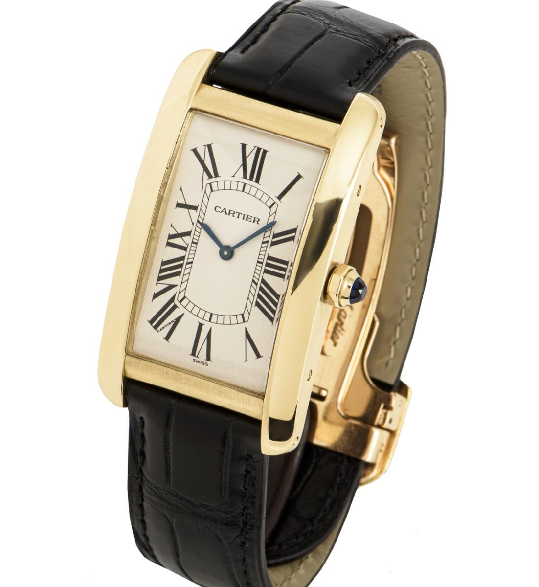 A 27 mm yellow gold Tank Americaine by Cartier. Features a silver dial with Roman numerals, sword-shaped hands in blued steel and a secret Cartier signature at V of VII. The faceted crown is set with a synthetic spinel.

An original deployant clasp