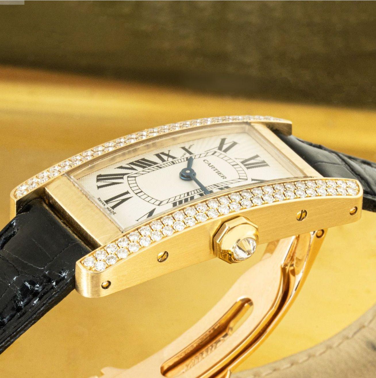 A 19mm Cartier Tank American crafted in yellow gold. Featuring a silver dial with roman numerals, blued-steel sword-shaped hands and a secret Cartier signature at 'X'. Complimenting the dial is a yellow gold bezel set with 98 round brilliant cut