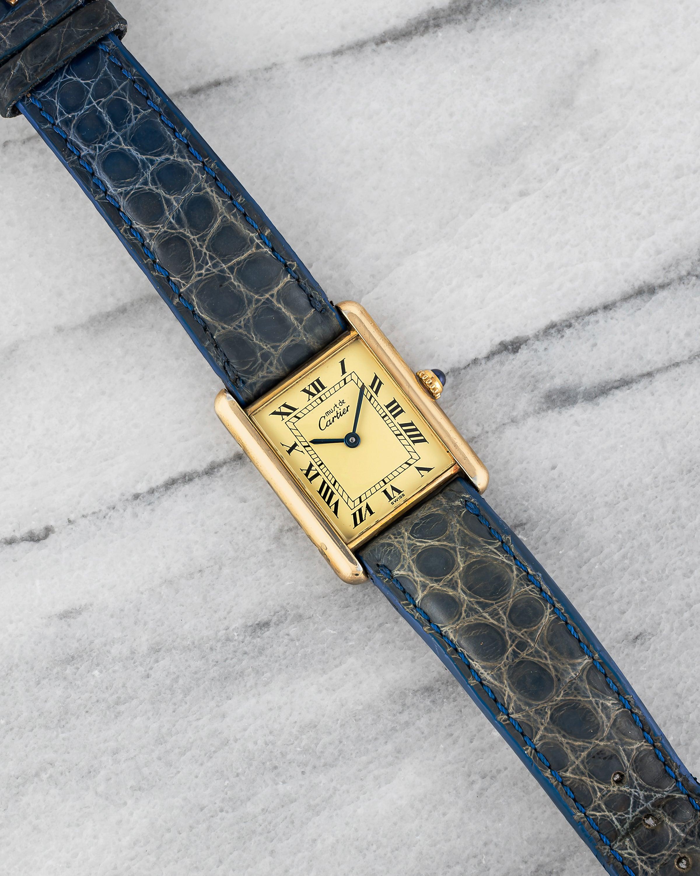Aquí tienes un Must de Cartier vintage de cuerda manual con esfera de números romanos limón de finales de los 70, principios de los 80. Mantiene la hora y es totalmente funcional. Las medidas incluyen un tamaño de la caja de 23x30 mm y una anchura