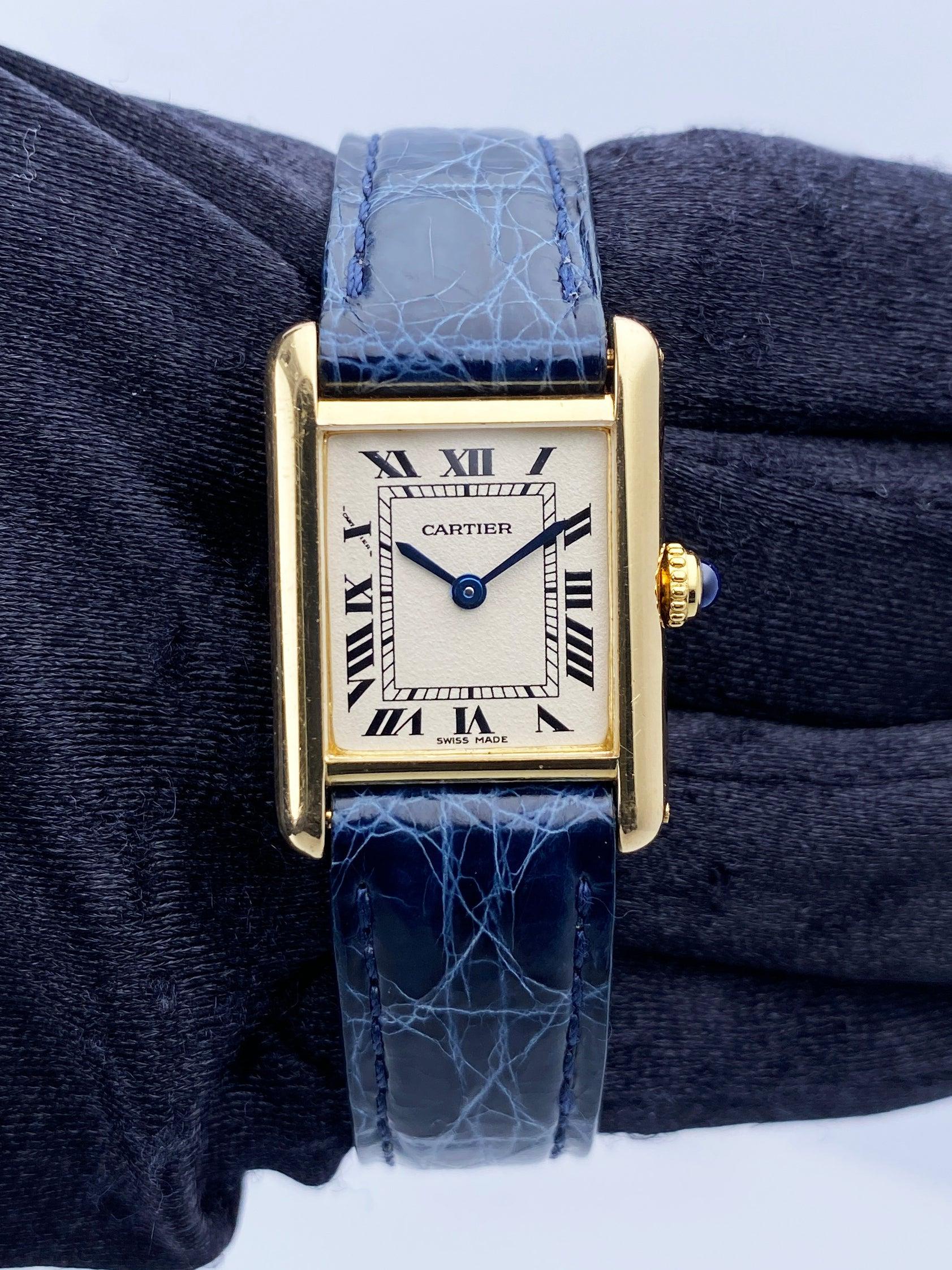 Montre pour femme Cartier Tank Louis W1512753. Boîtier de 21 mm en or jaune 18K. Cadran blanc cassé avec aiguilles bleues et index noirs en chiffres romains. Index des minutes sur le cadran intérieur. Bracelet en cuir bleu avec boucle en or jaune