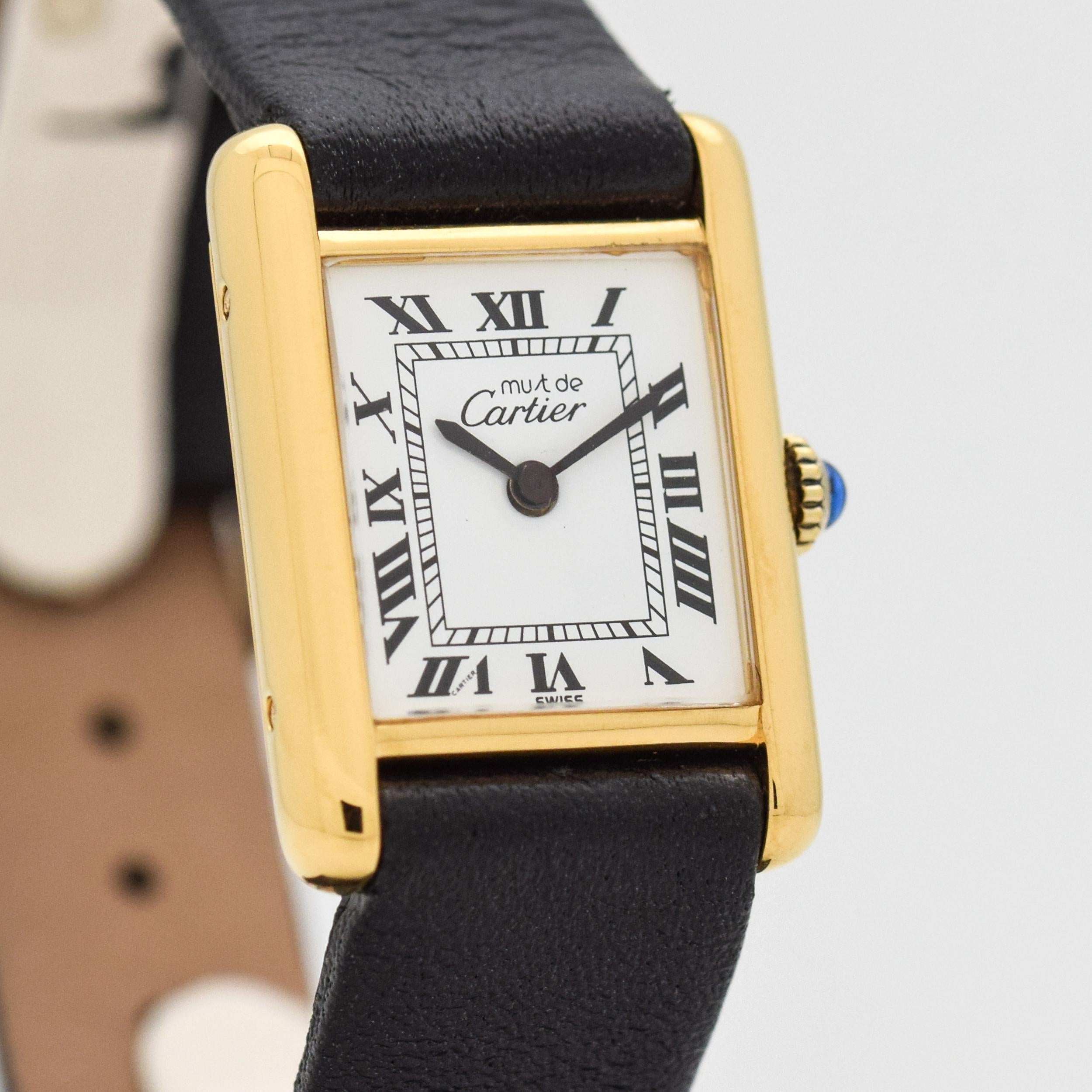 1990's era Cartier Tank Must de Ladies Watch. 18K Yellow Gold Plated over Sterling Silver example. White dial with black-colored, Roman numerals. Powered by a 17-jewel, manual caliber ETA movement. Equipped with a Genuine Calf Leather Black-colored